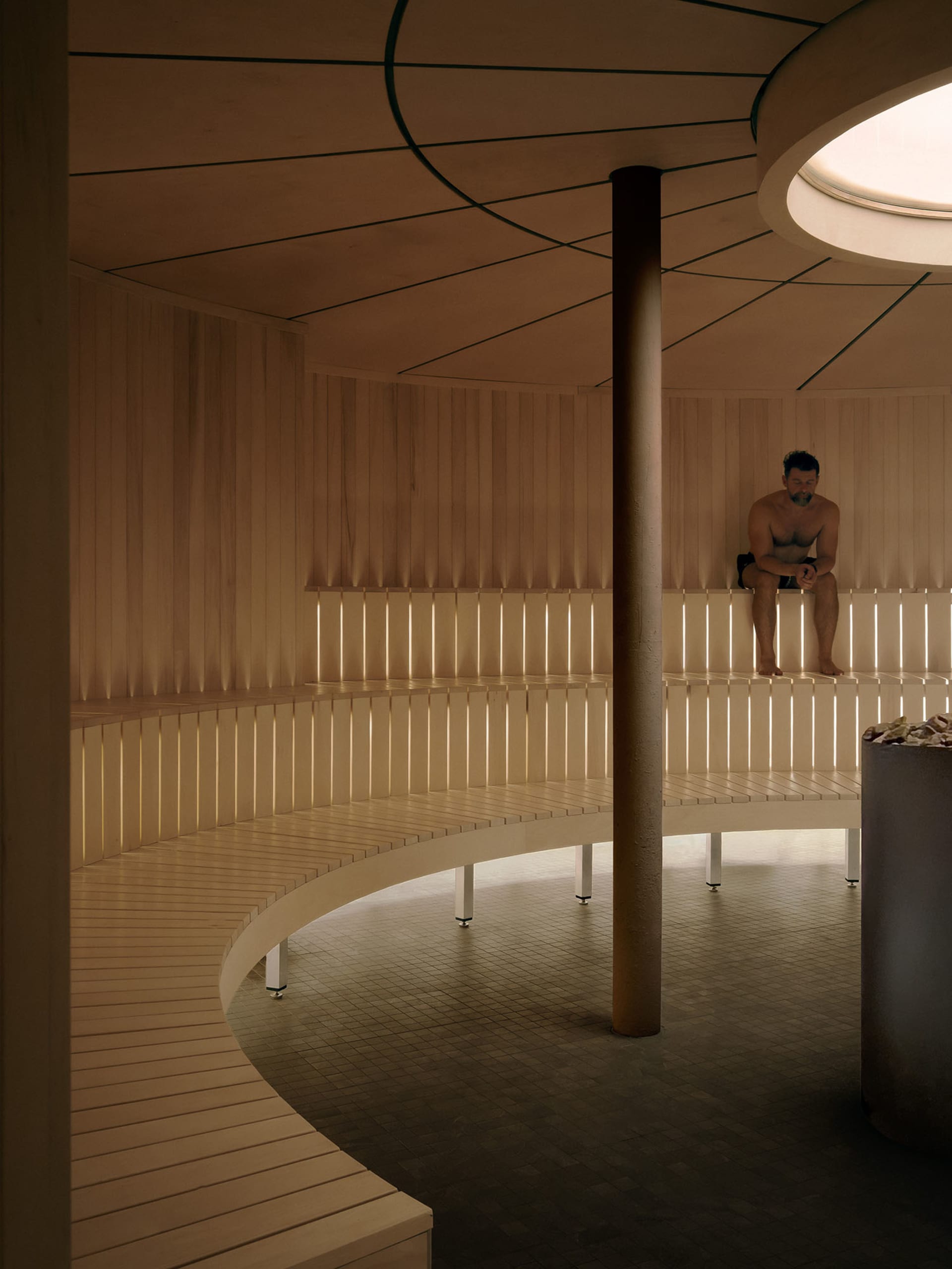 A man sits on a wooden bench in a calm and relaxed room with a pillar and wooden structure