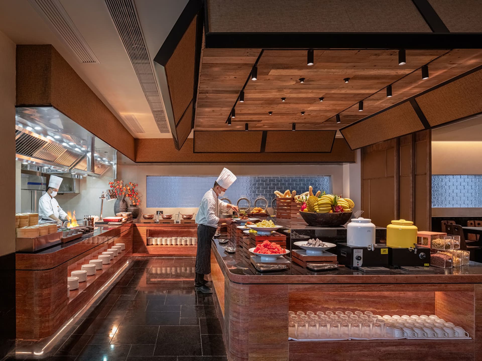 A busy kitchen with a chef preparing food in front of a wooden counter with various fruits and bowls of food on it