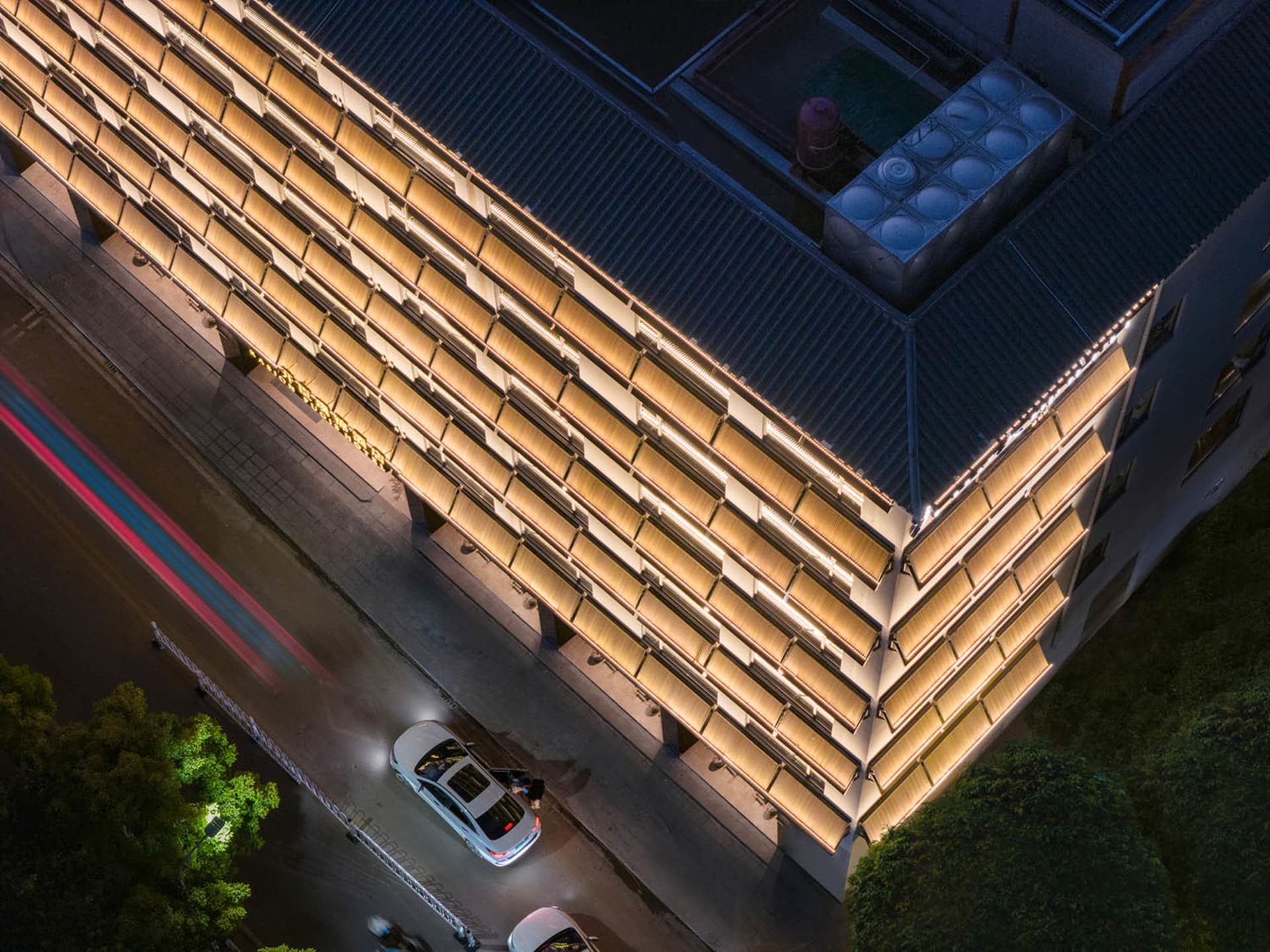 A large building at night with artificial lighting, set against a dark city sky with parked cars in front