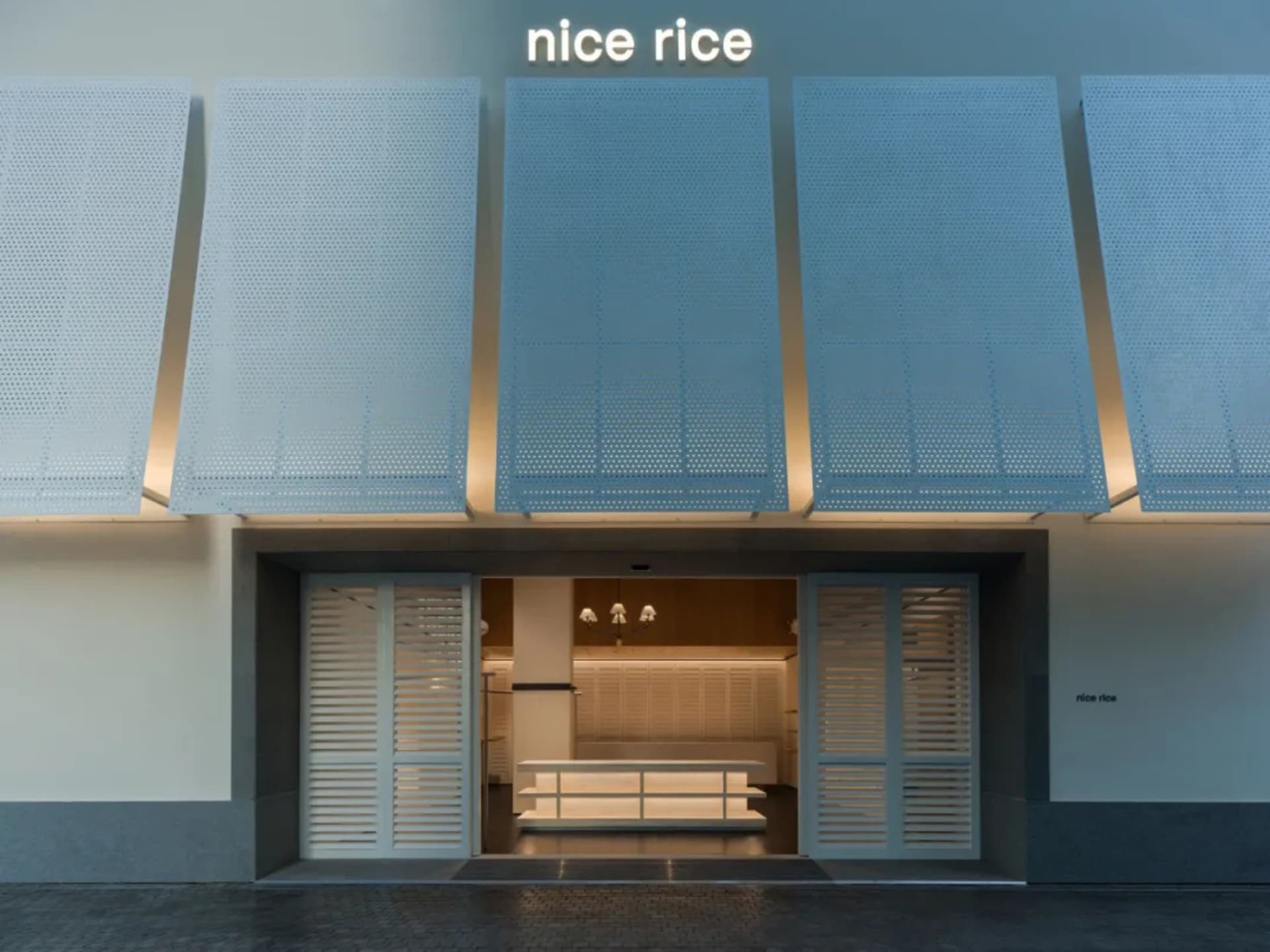 A storefront with a white and blue color scheme, featuring a large window, metal awning, and a sign reading Nice Rice