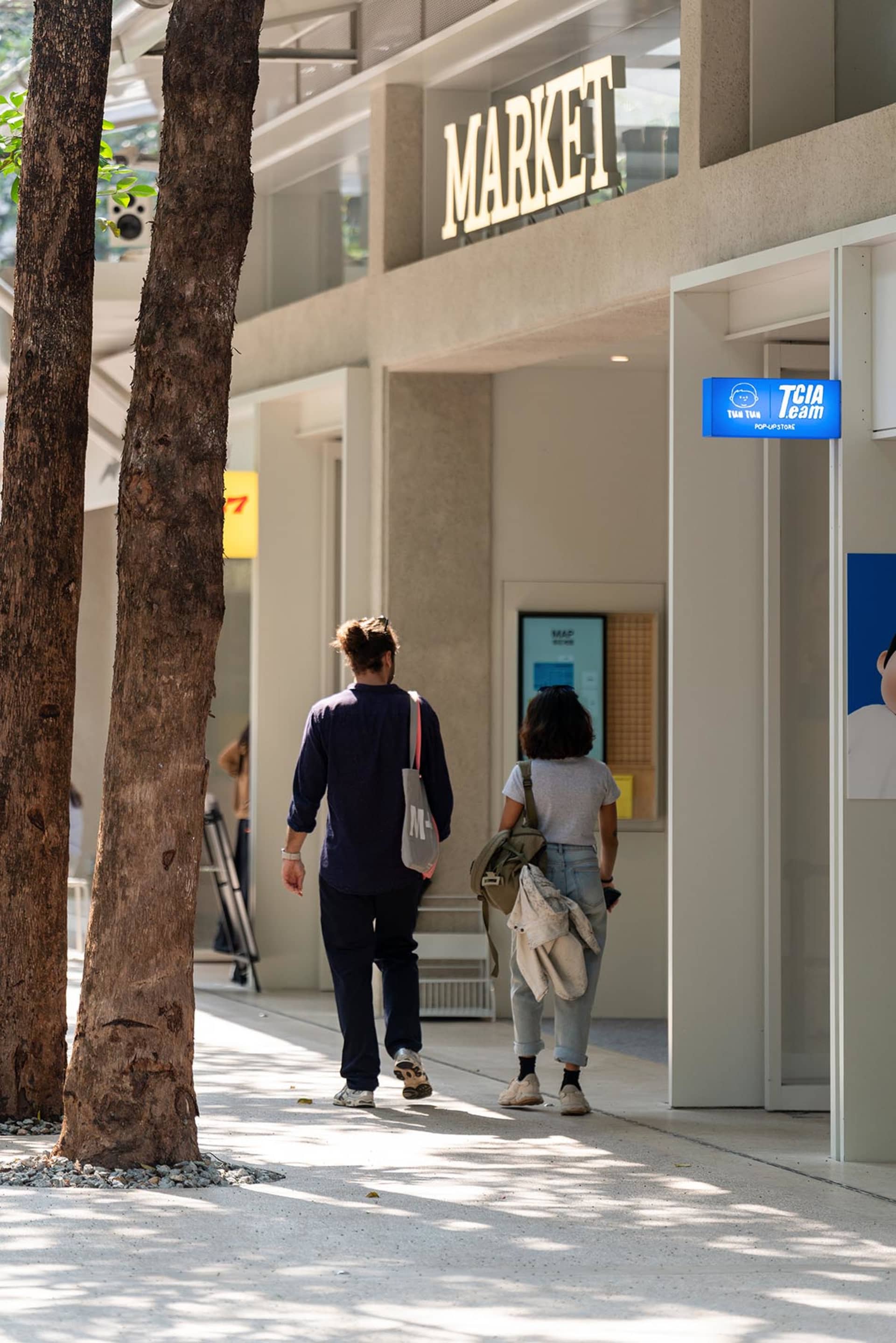 A casual urban scene with a couple walking down a sidewalk in front of a building, with the building and sidewalk as the main elements visible
