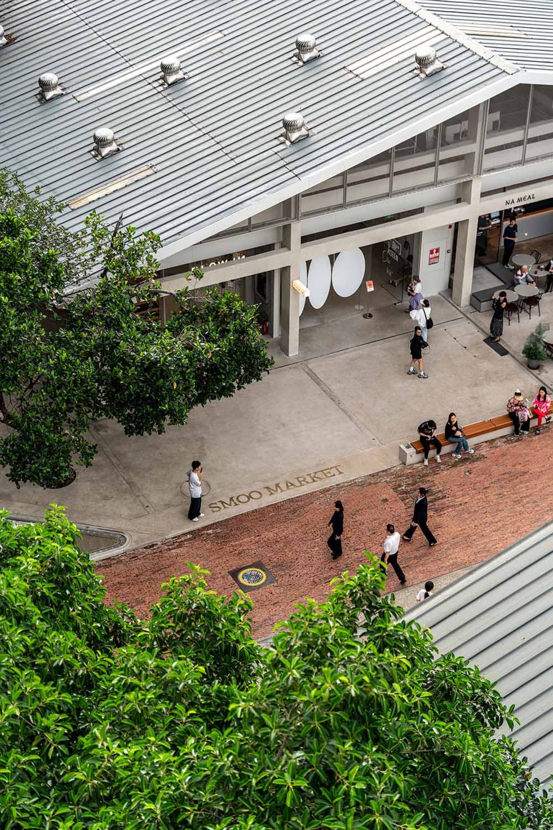 A brick walkway in front of a market with people walking in various directions, carrying handbags, in a lively and bustling outdoor scene