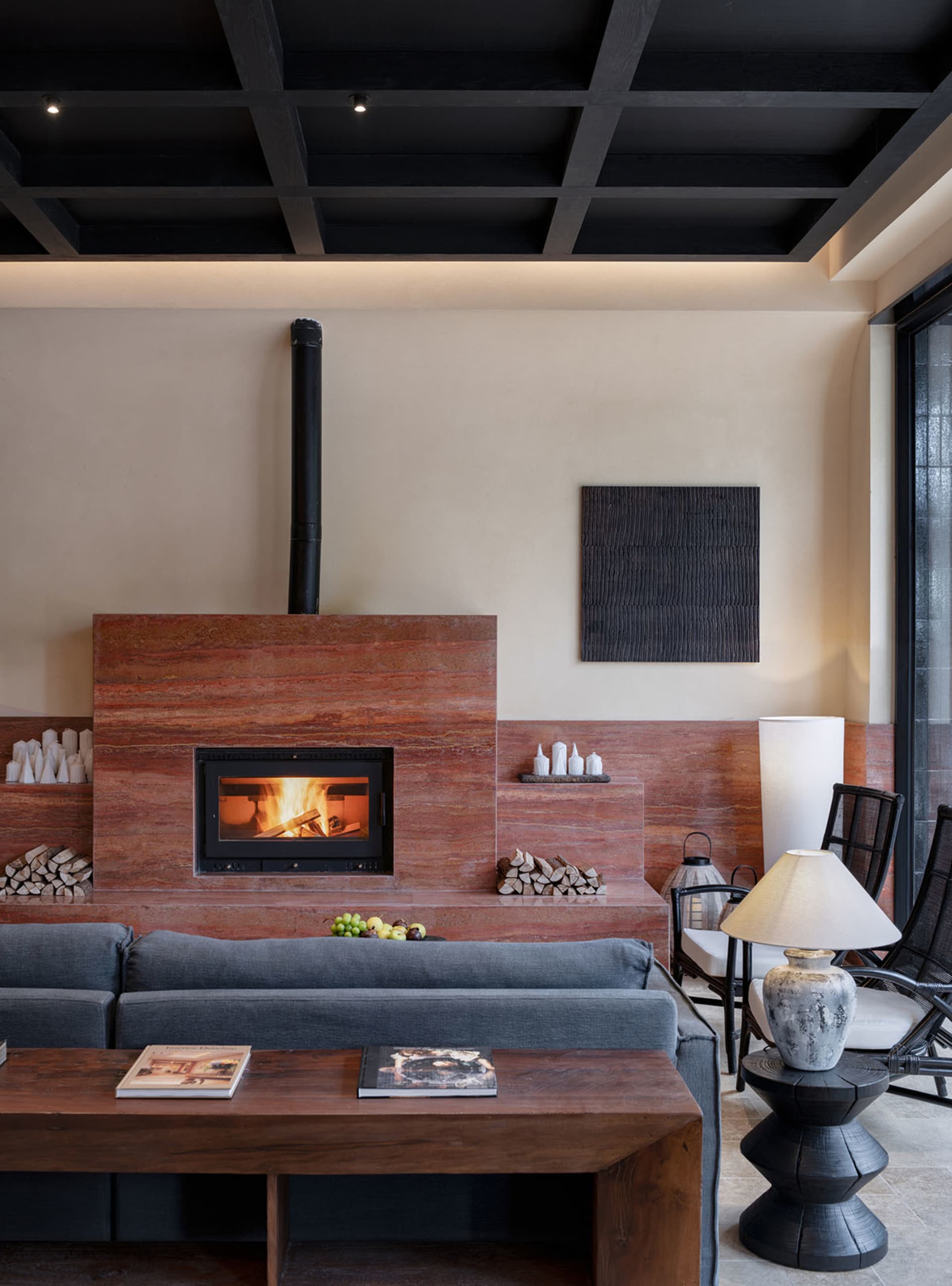 Cozy living room with a fireplace, couch, chair, and dining table, decorated with books, vases, and bottles, with dim warm lighting