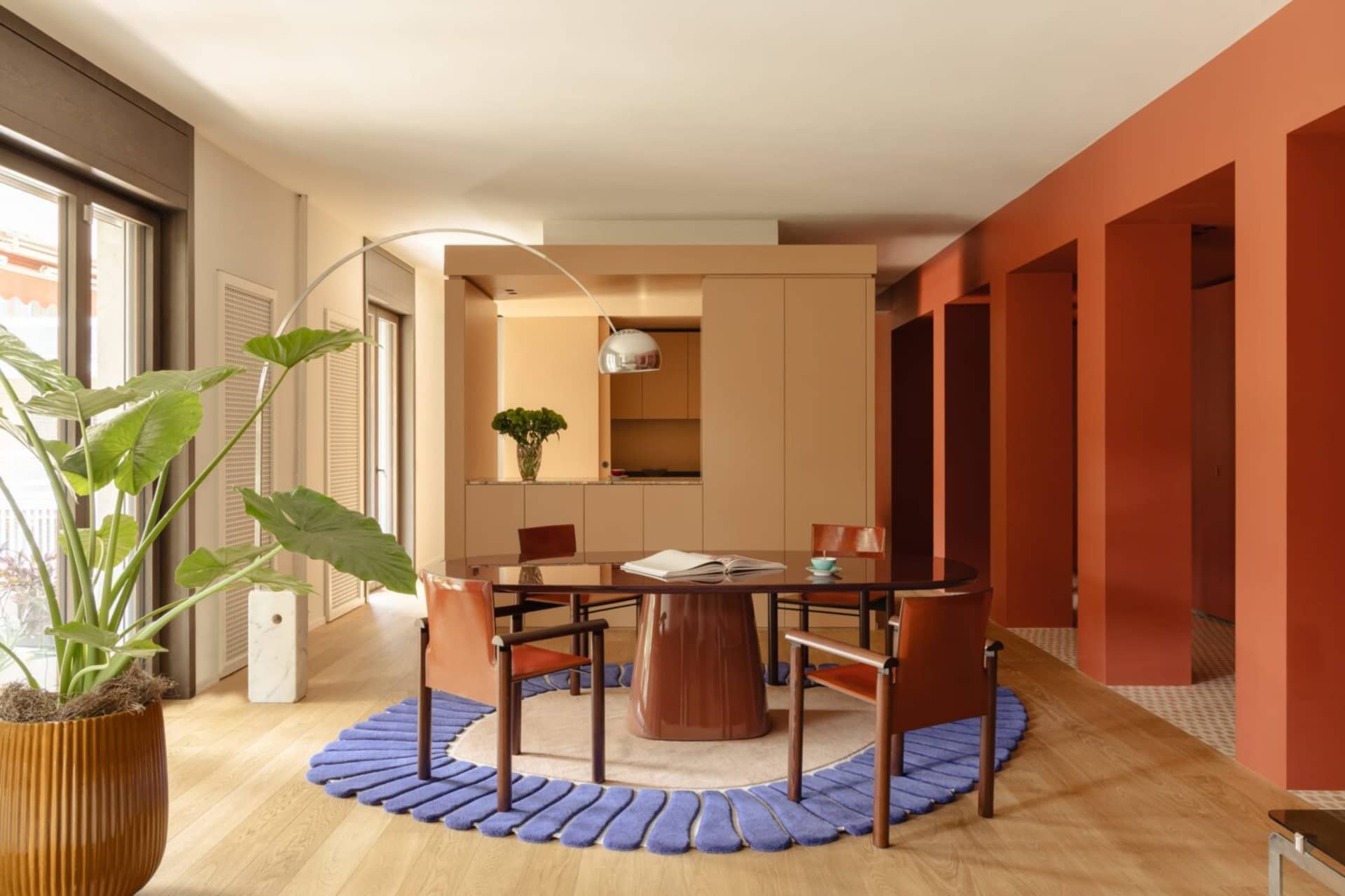A well-lit living room with a wooden floor, a dining table, chairs, a potted plant, and a vase, creating a cozy and inviting atmosphere