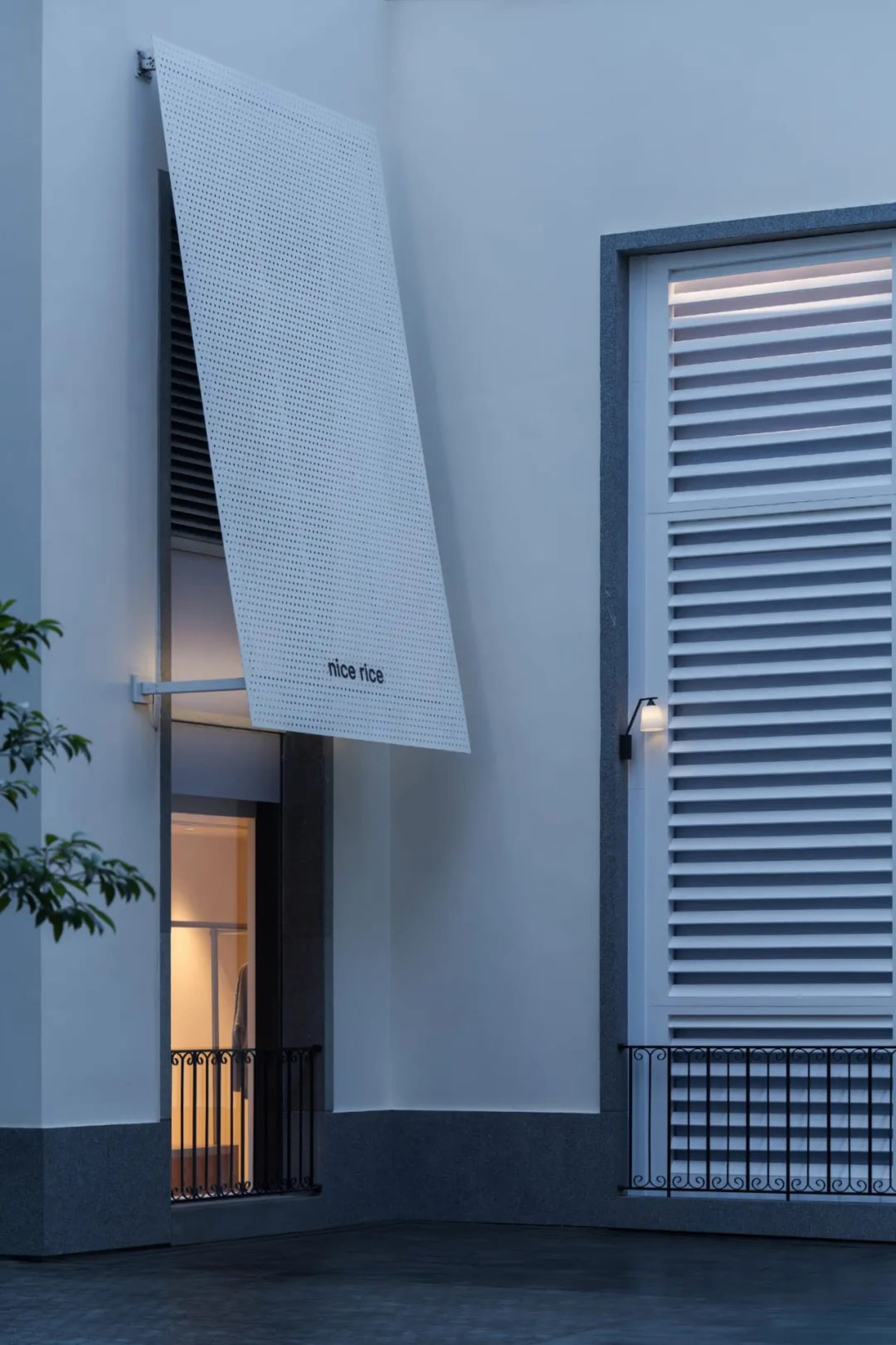 Photograph of a commercial building with a white concrete facade, a large window, and a white awning, taken in dim lighting