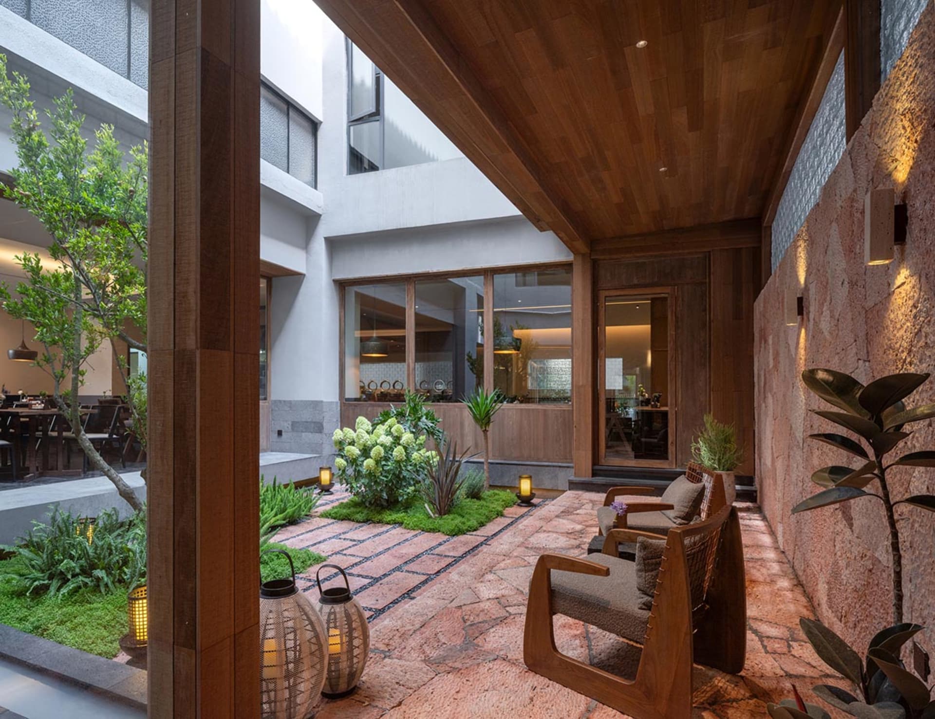 Open living room with a wooden floor, natural light, and modern furniture, including a couch, chair, and dining table, with a potted plant adding greenery