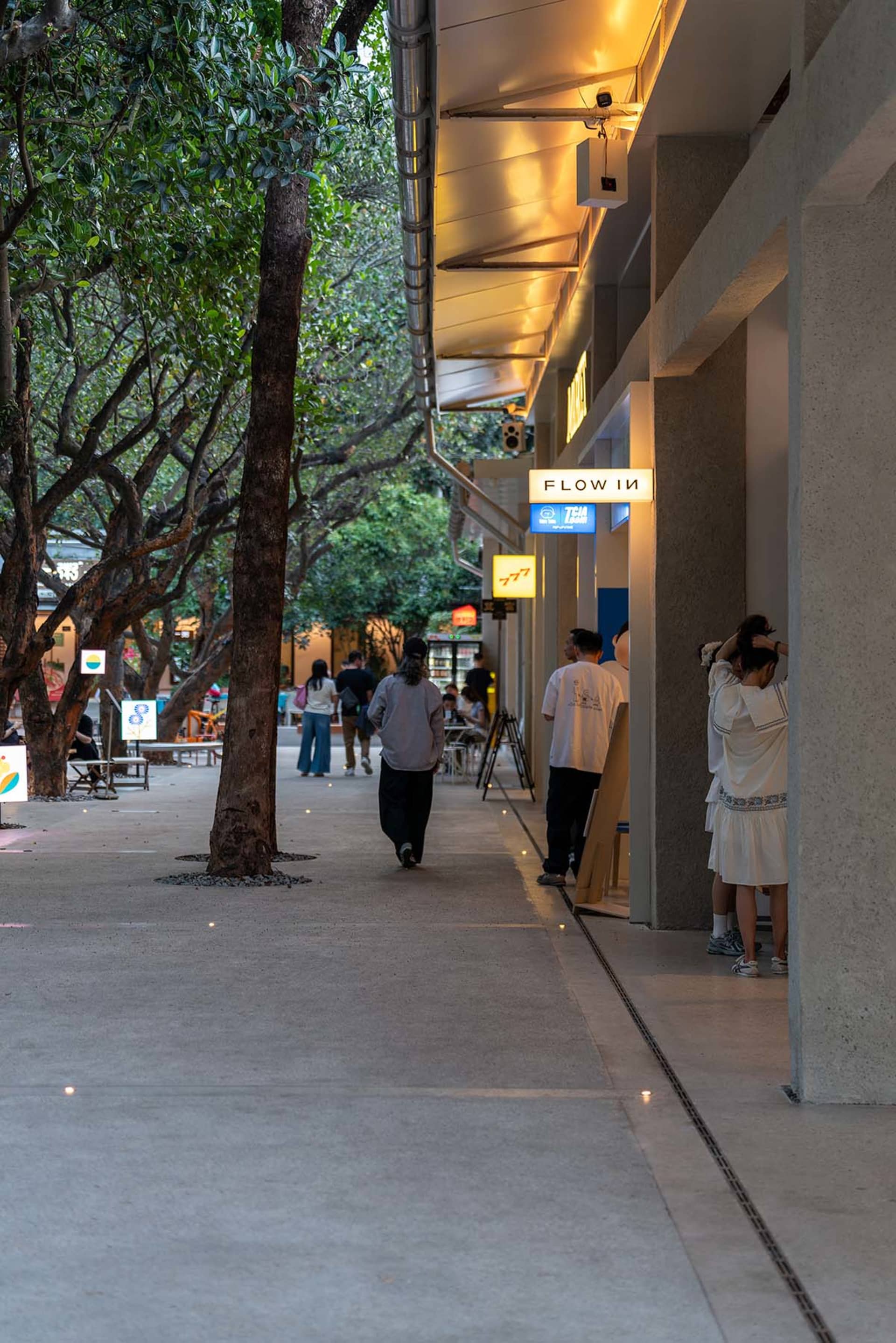 A bustling shopping street with people walking in various directions, surrounded by trees and lined with buildings