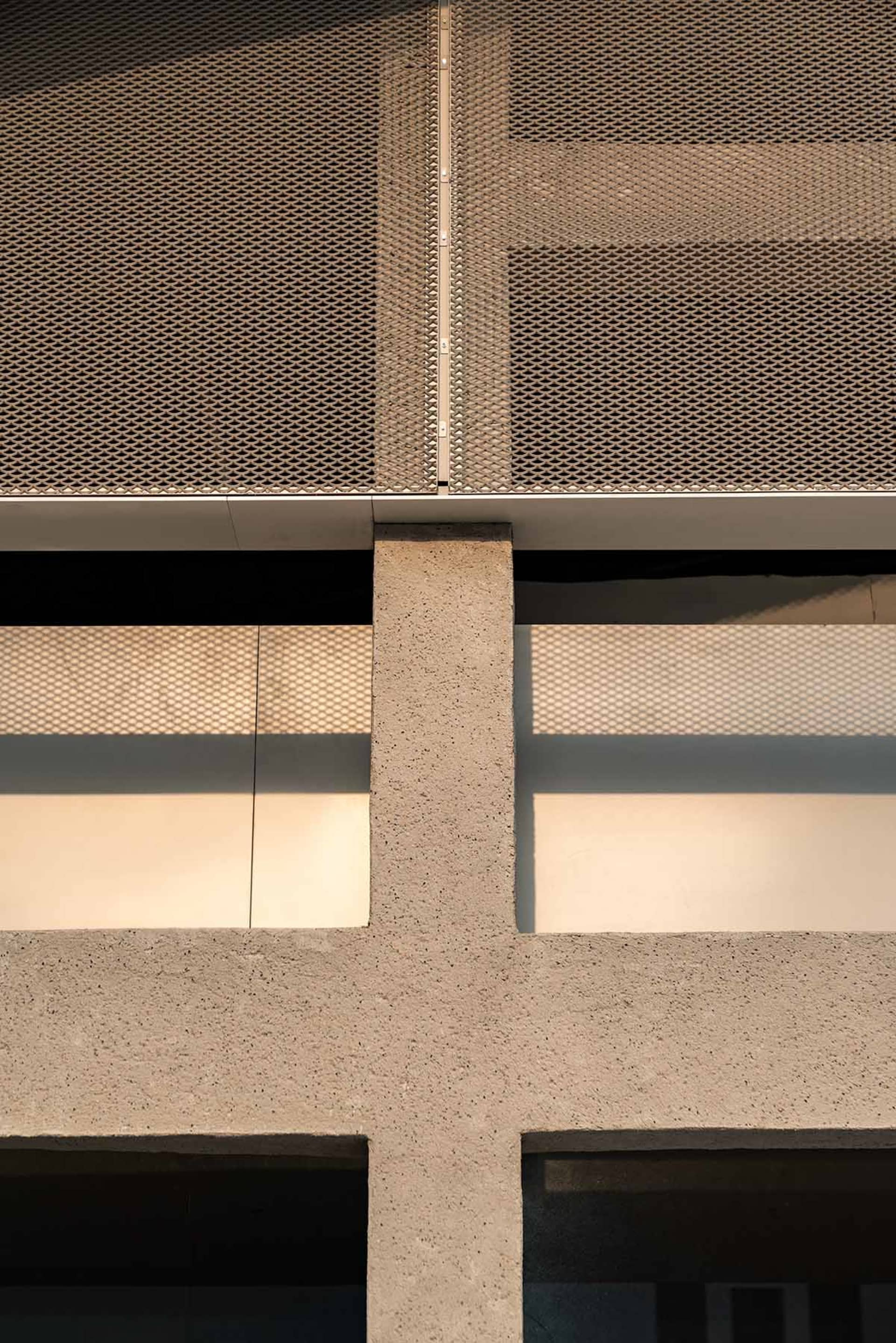 Grey concrete building with a metal fence attached to the wall, set against a bright and open background