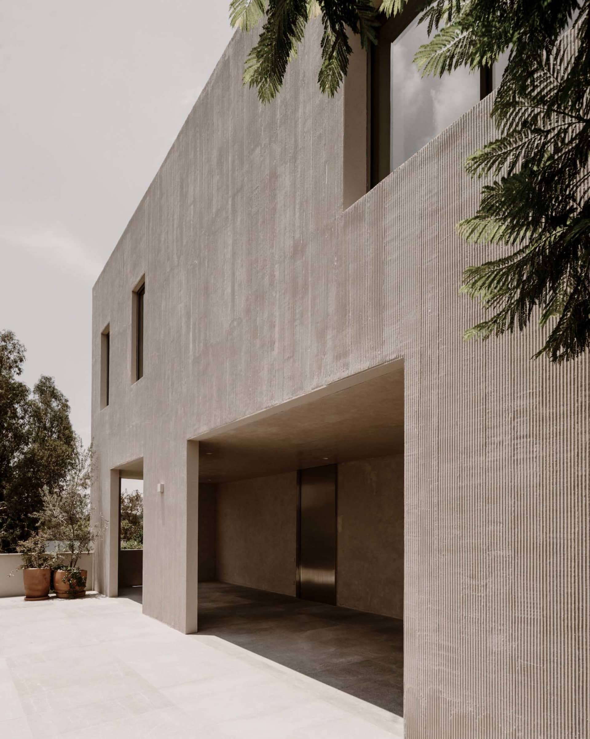 Photograph of a modern building with a concrete exterior, featuring a large window and door, and a sleek contemporary design