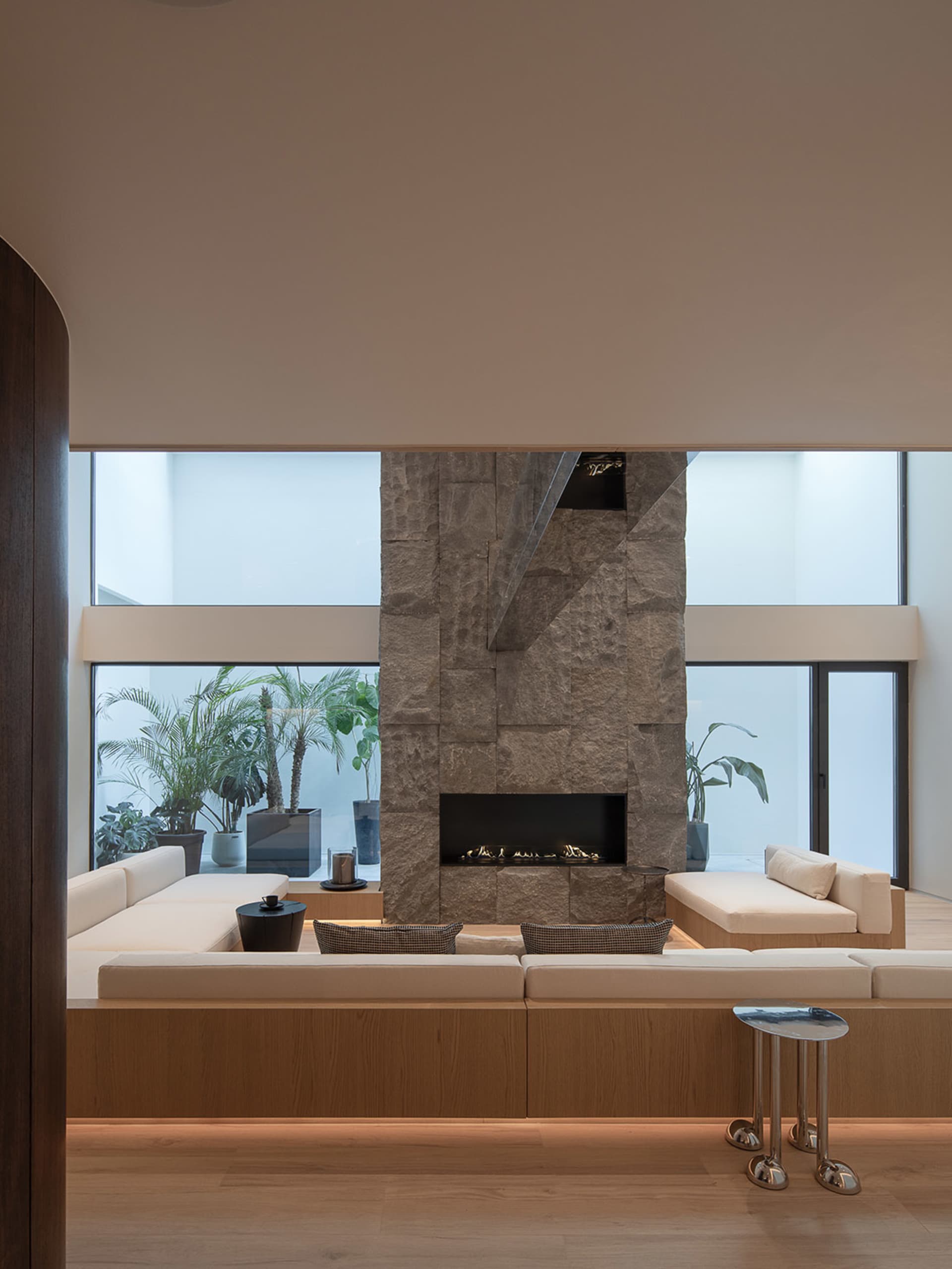 Cozy living room with a stone fireplace, wood furniture, and a potted plant, featuring natural light and a warm atmosphere