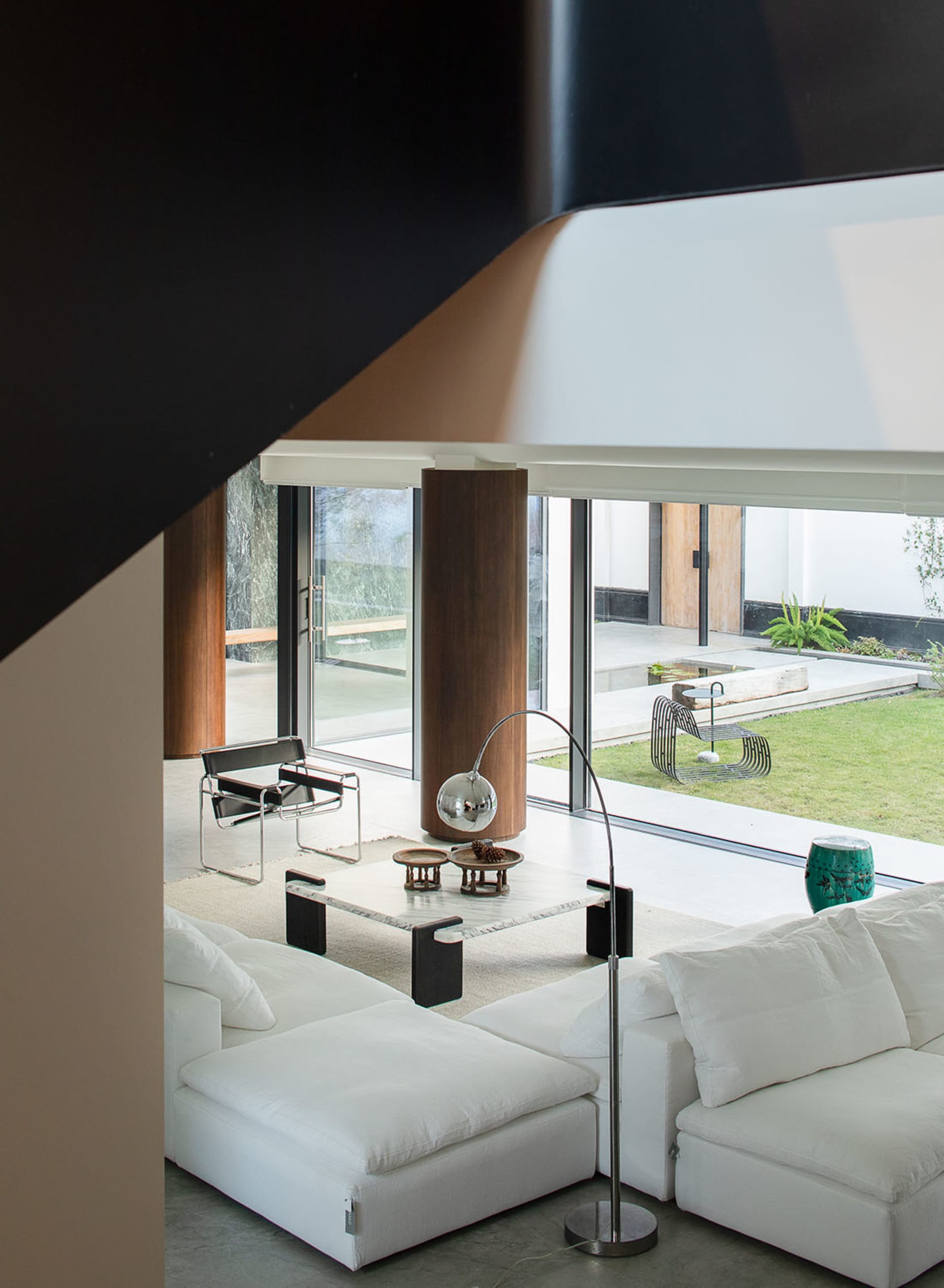A well-lit living room with a large window, a white couch, a chair, and a dining table, giving a clean and minimalist appearance
