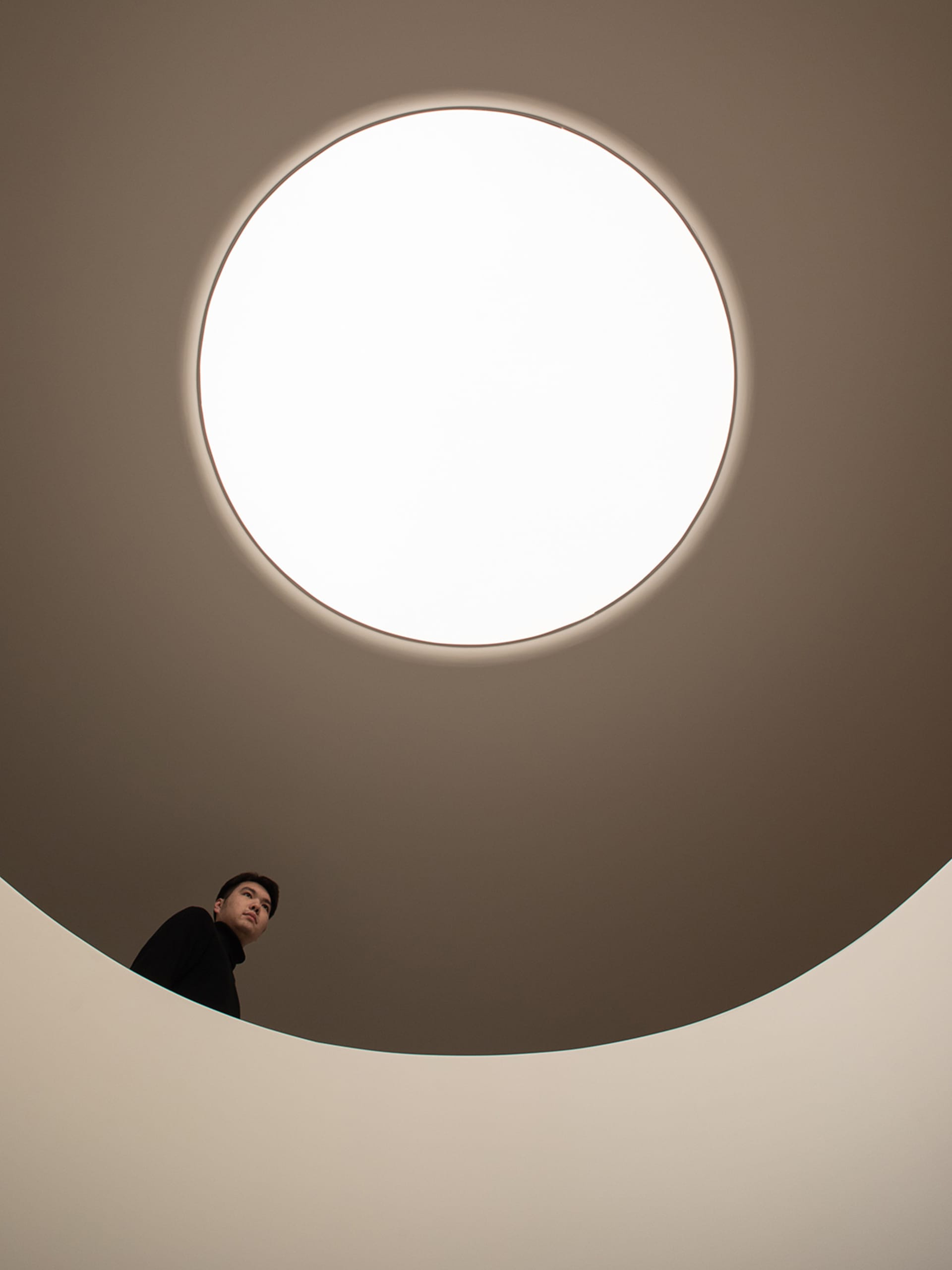 一位男子站在大型圓形白色燈具下，位於具圓形設計與乾淨美學的現代極簡空間