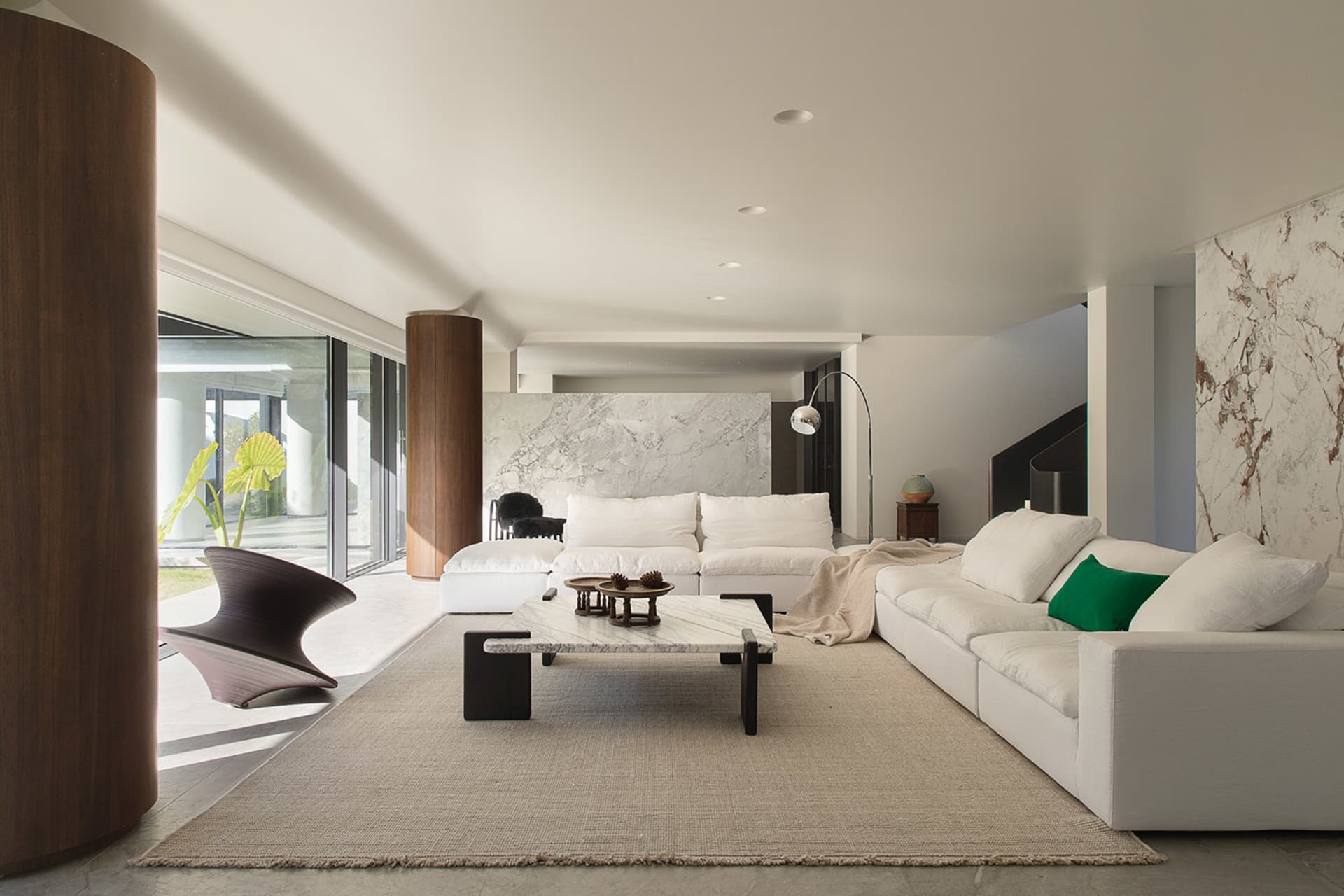 A modern living room with a white couch, chair, and coffee table, surrounded by various decorative items and natural light from the windows