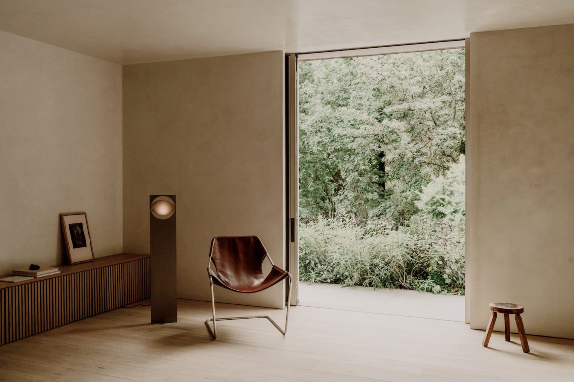 Cozy living room with a brown leather chair, lamp, and natural light from a large window, decorated with potted plants