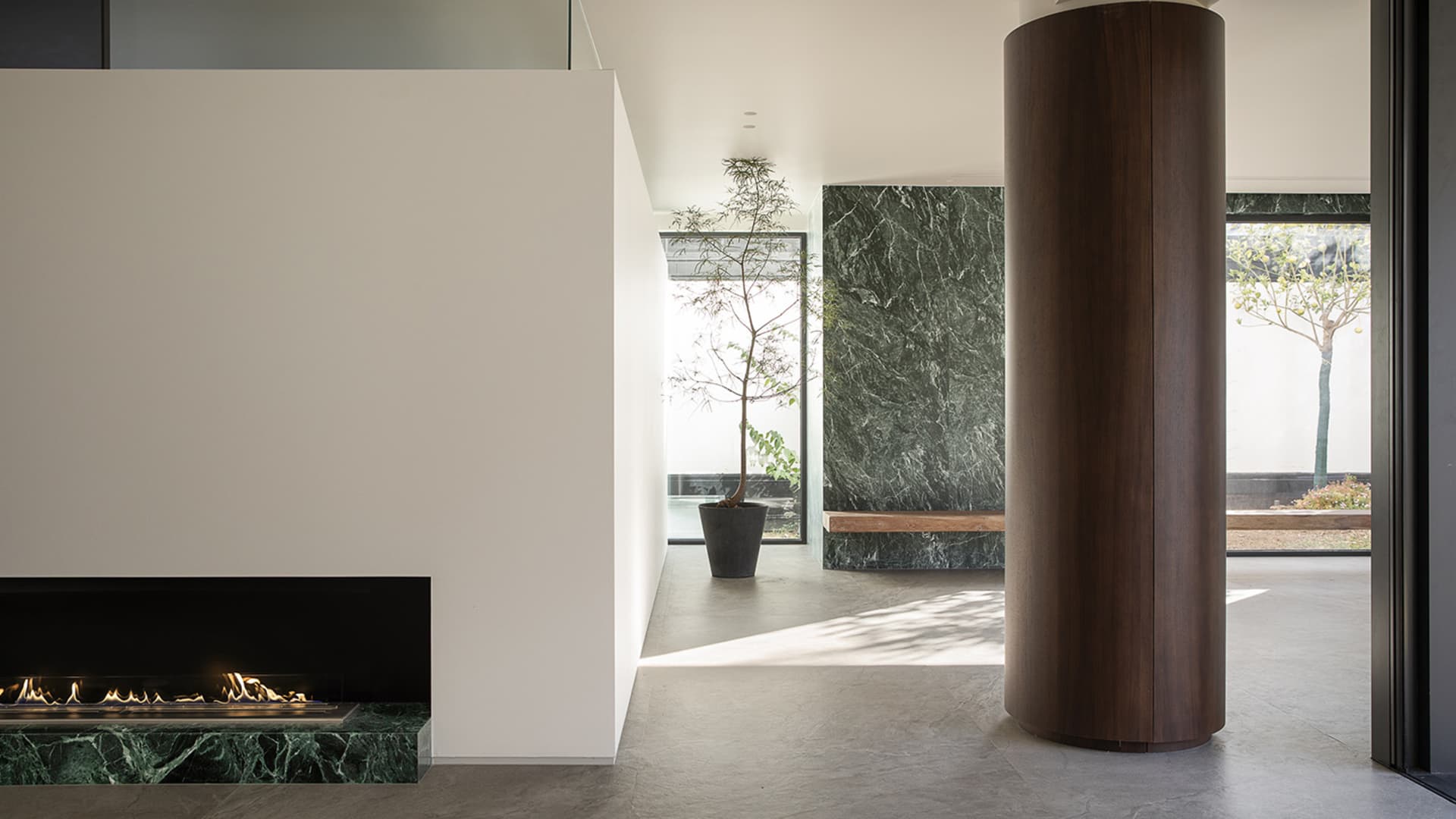A modern living room with a predominantly white color scheme, a stone wall, a fireplace, and a potted plant, well-lit by natural light through the windows
