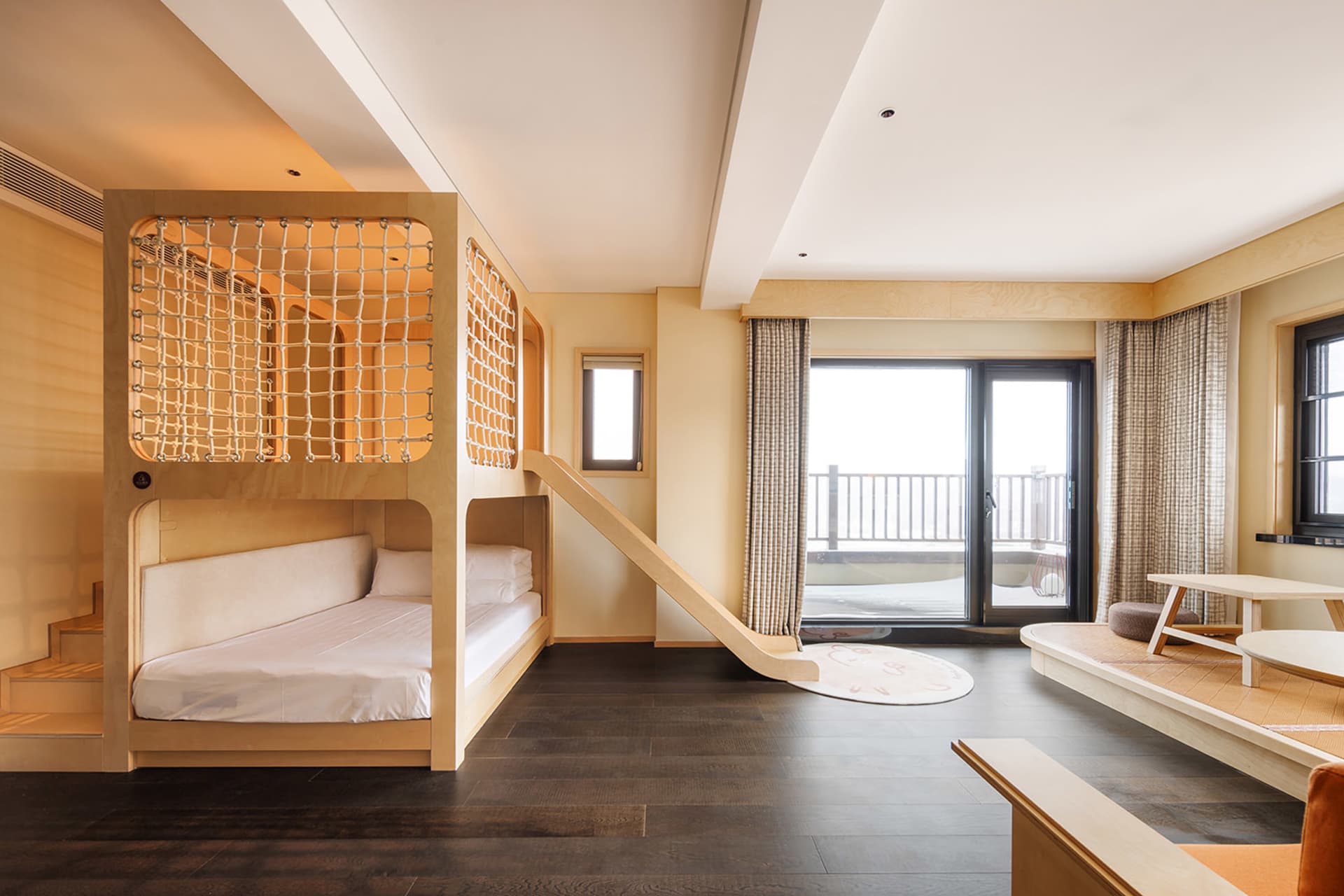 Cozy modern bedroom with a wooden floor, a bed, chair, and couch, featuring natural light and a ladder leading to a higher level