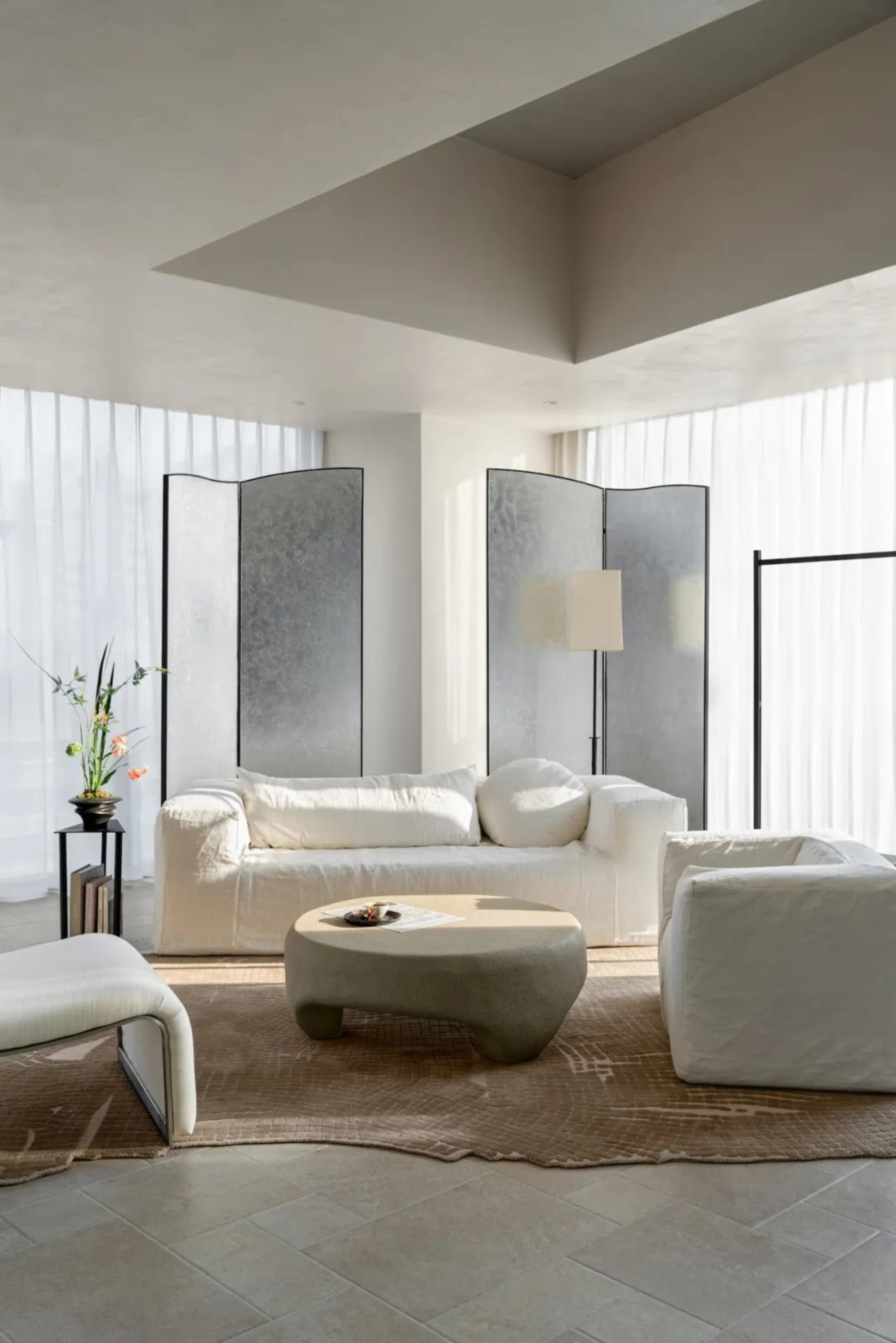 Well-lit modern living space with a white couch, chair, and coffee table, surrounded by natural light from windows