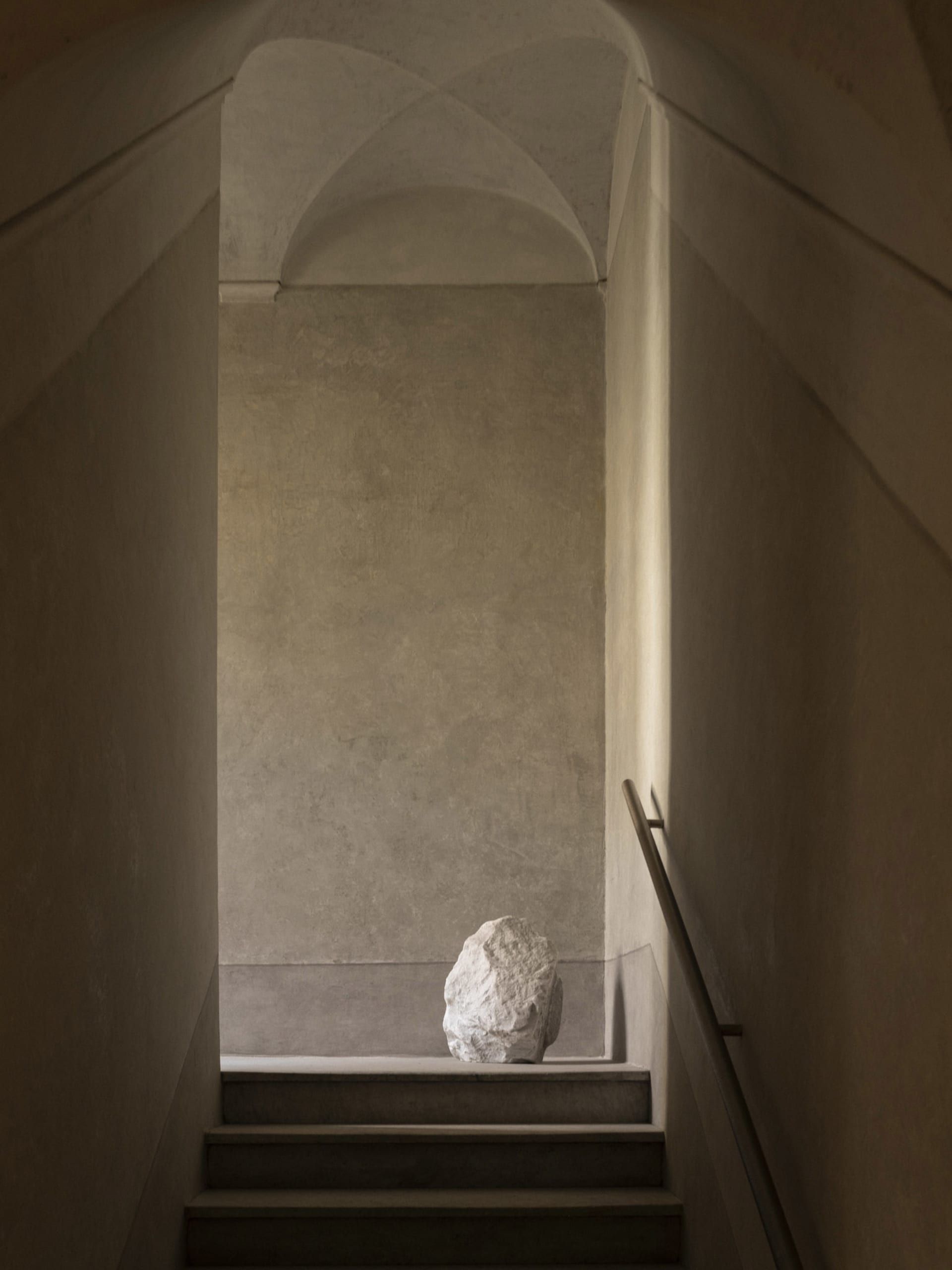 A traditional hallway with a stone staircase, stone wall, and stone column, set in a dimly lit space with a moody atmosphere