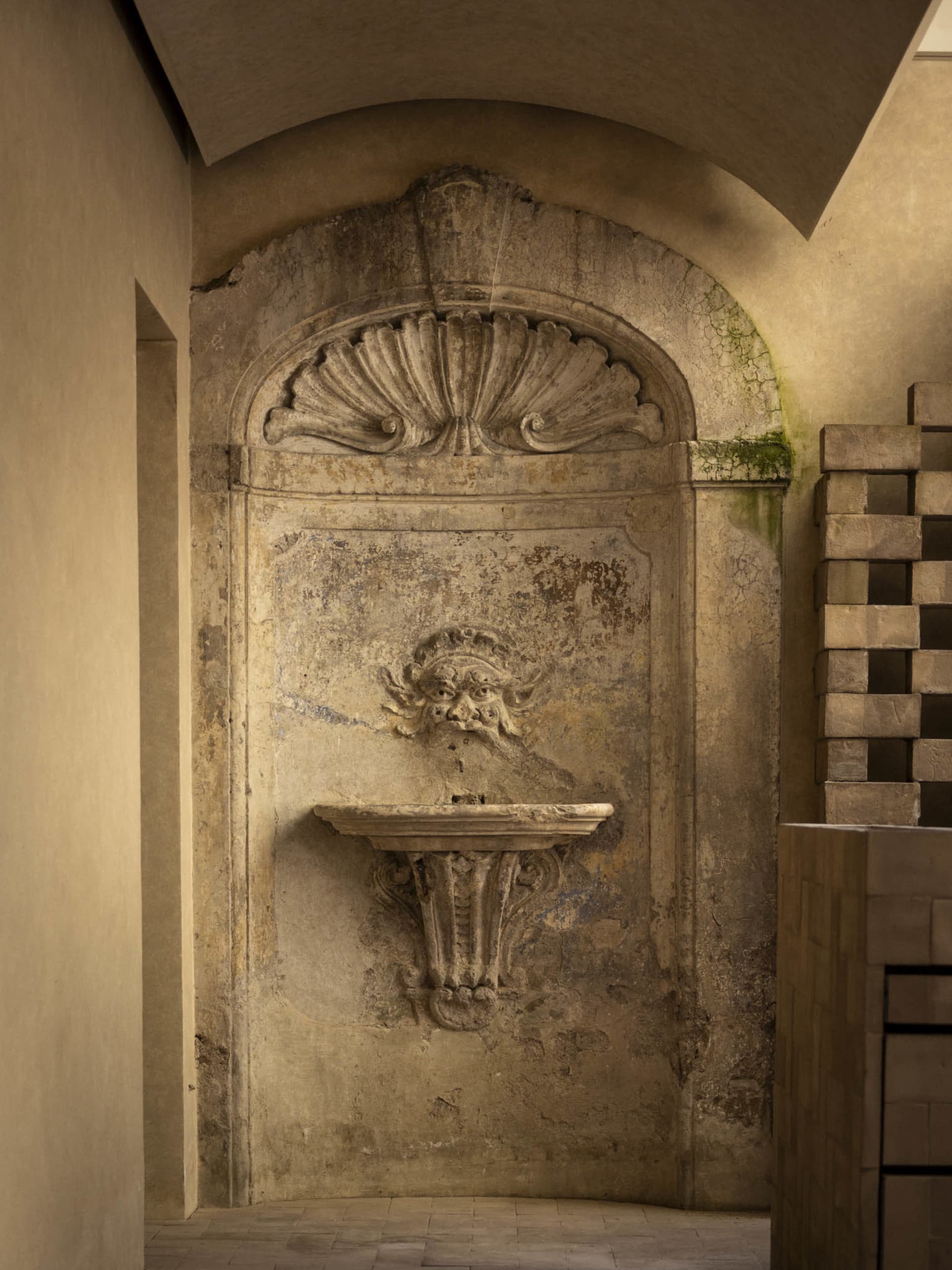 A stone wall with a built-in fountain, surrounded by a stone frame, in a dimly lit, old-fashioned setting