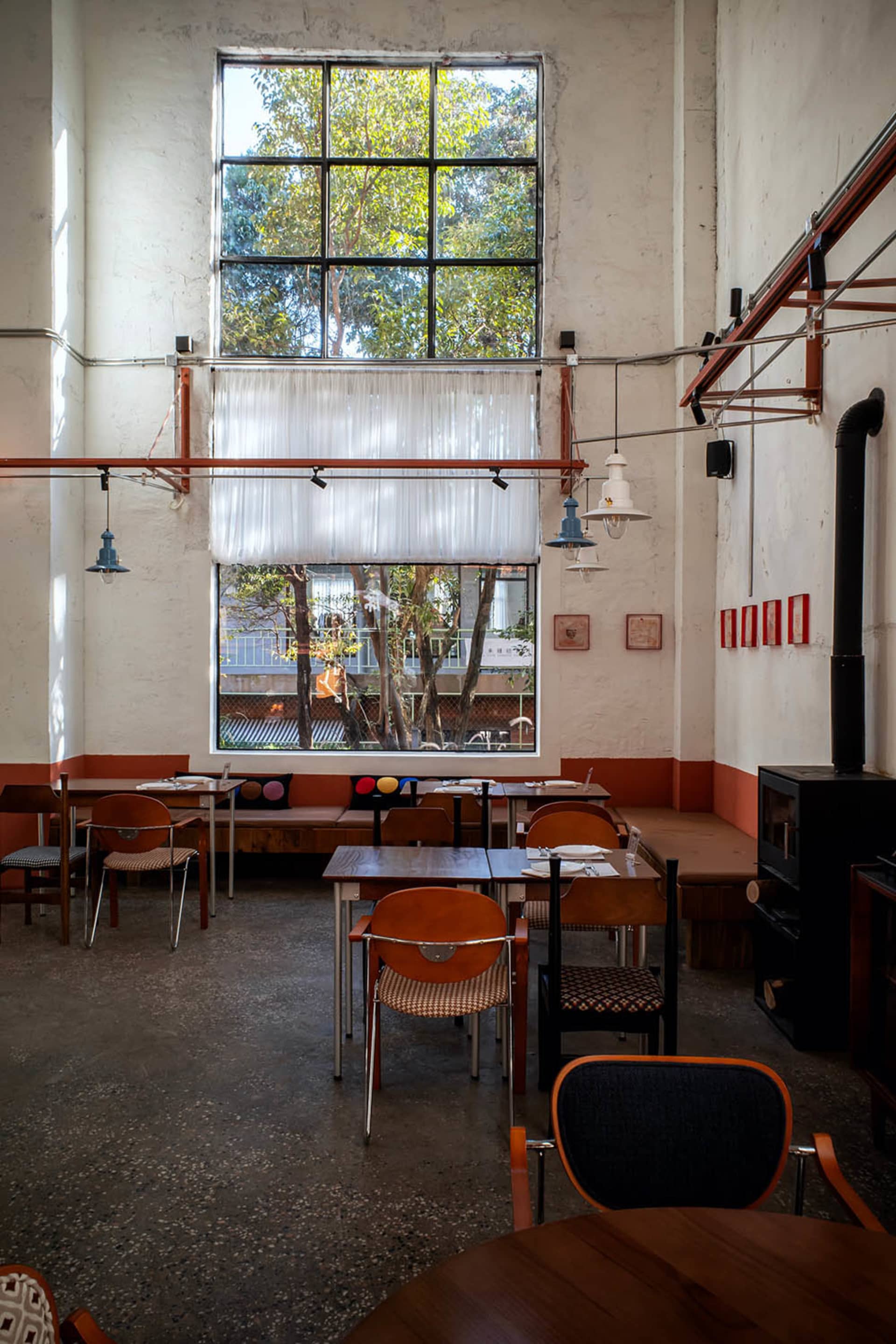 A cozy restaurant with a large window, wooden furniture, and a dining table, lit by natural light and warm sunlight