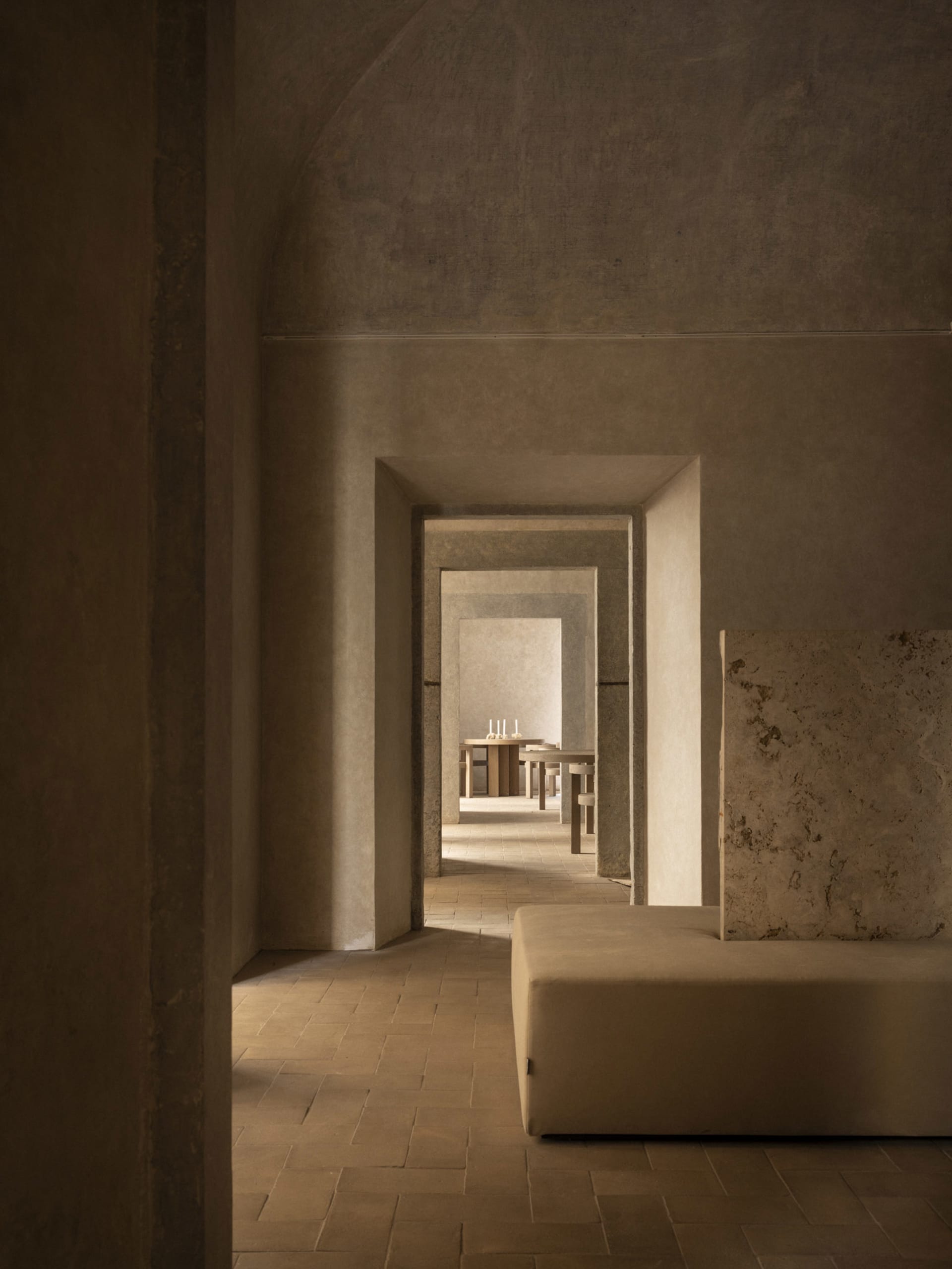 A dimly lit stone hallway with two benches and a dining table, featuring a simple and functional design with natural materials