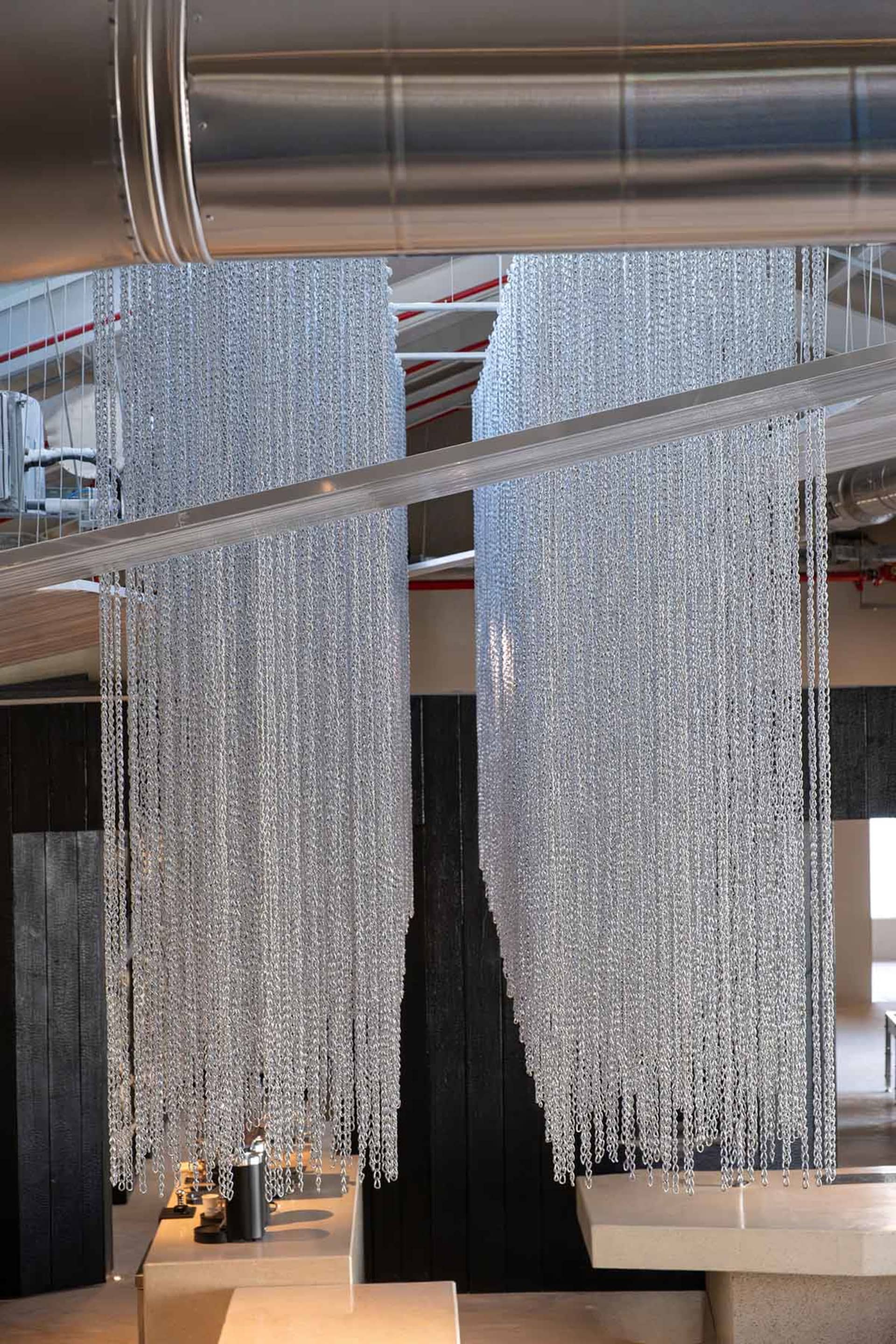 A dimly lit room with a black and white color scheme, featuring numerous chains hanging from the ceiling at various heights and angles, creating a modern and minimalistic atmosphere