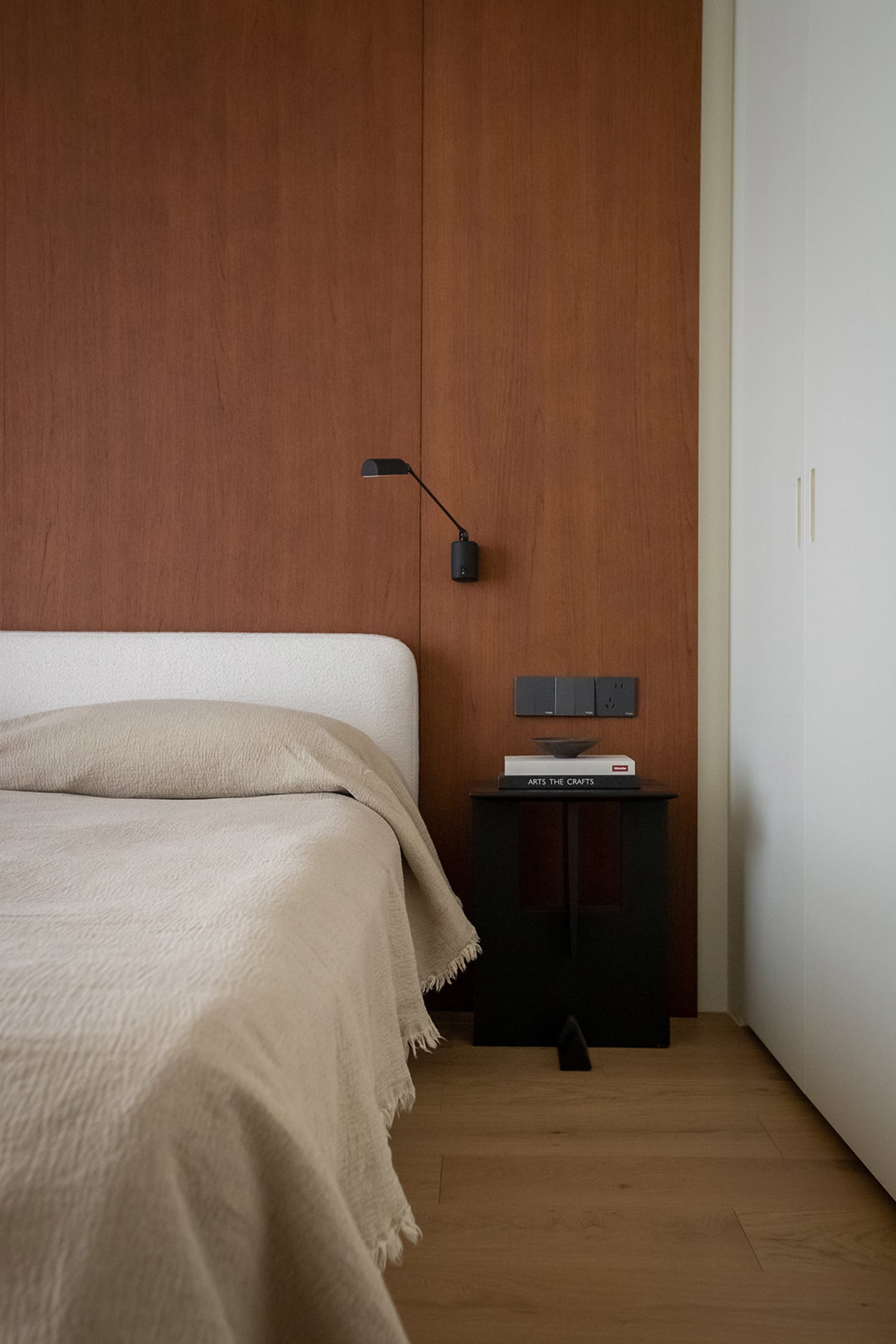 A well-lit modern bedroom with a white-covered bed, a wooden bed frame, and a metal nightstand with a lamp, set against a white background