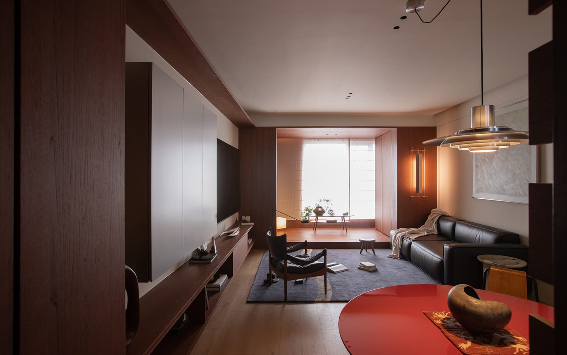 Cozy modern living room with a red table, a couch, a chair, and a TV, decorated with a vase, a bowl, and a book, with natural light and a warm atmosphere