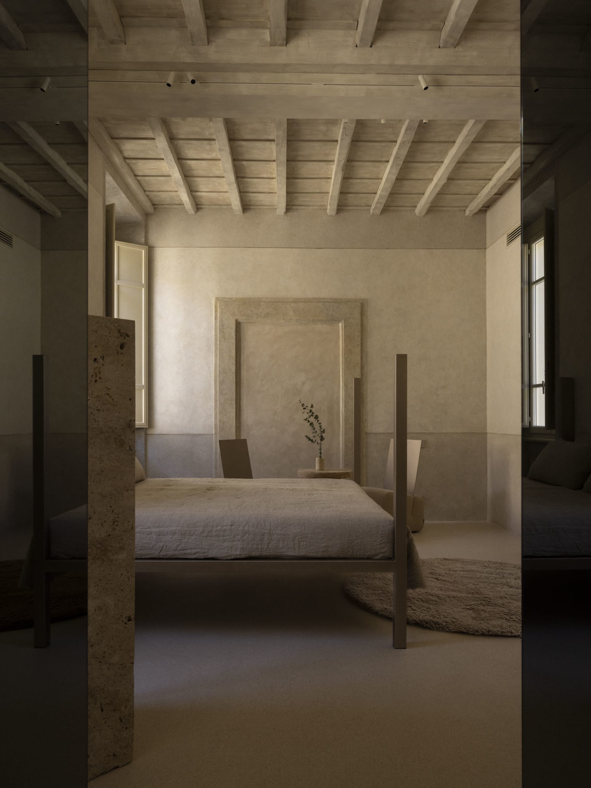 Cozy bedroom with a stone wall, wooden floor, a bed, and a chair near a window, dimly lit