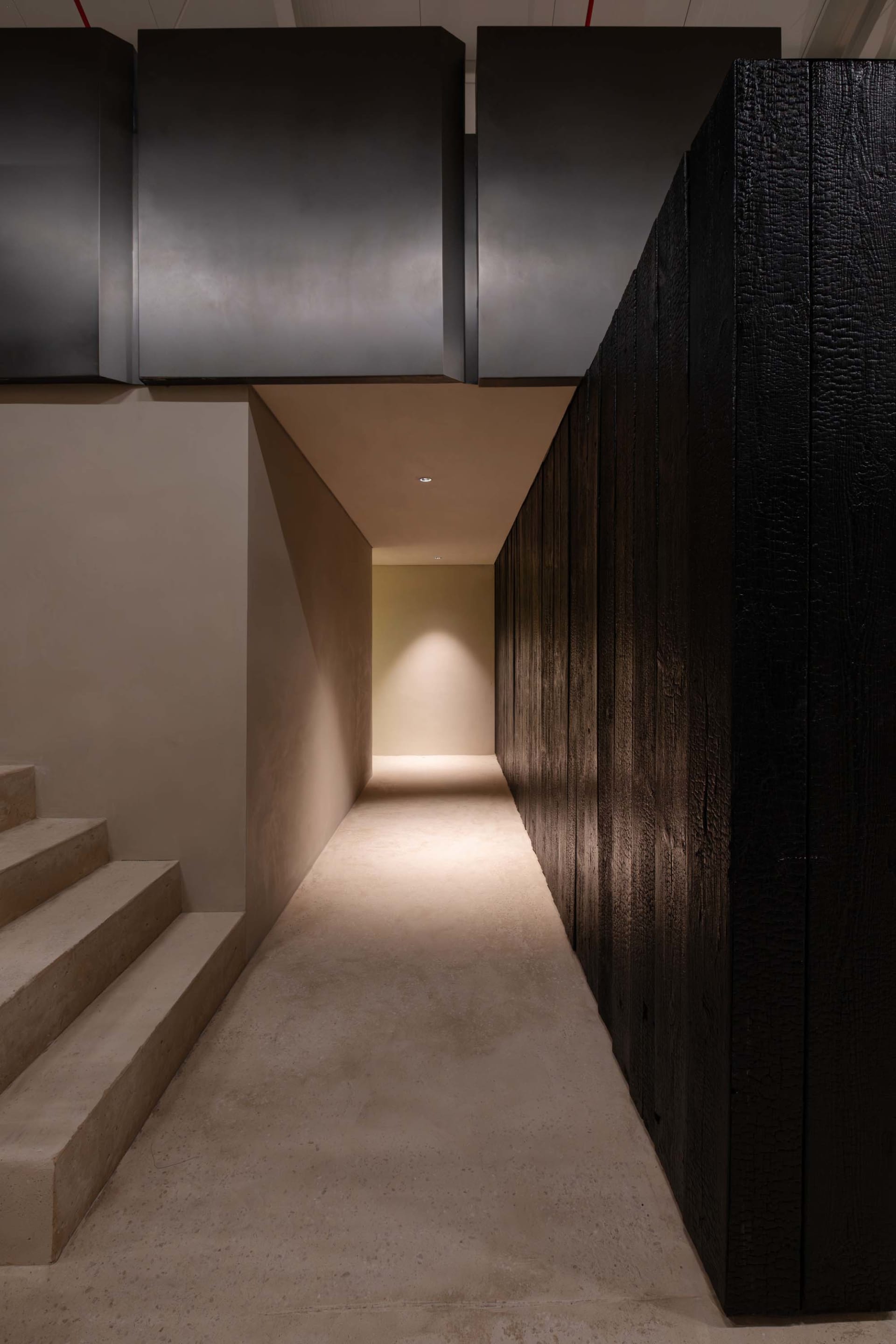 A dimly lit hallway with a concrete floor, metal railing, and a doorway leading to a room with a yellow wall