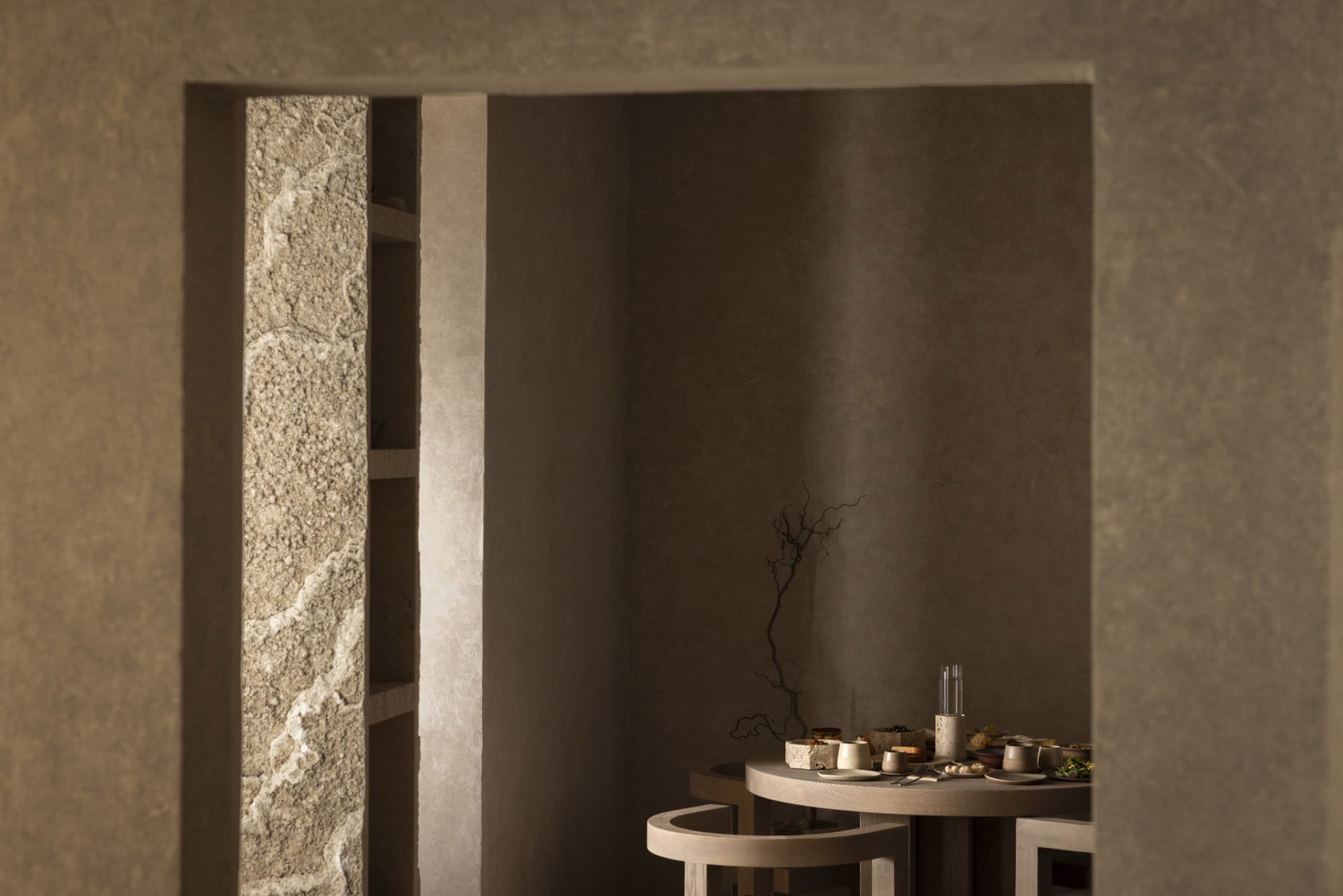 Cozy dining area with a stone table and chairs, surrounded by stone walls, with dim lighting and warm wood accents