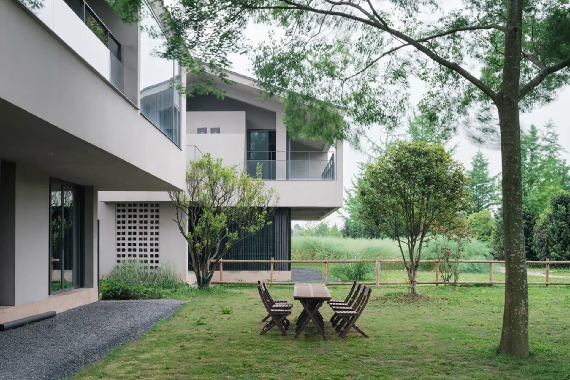 A modern outdoor dining space with a wooden table and chairs, surrounded by a house with a covered patio and natural sunlight
