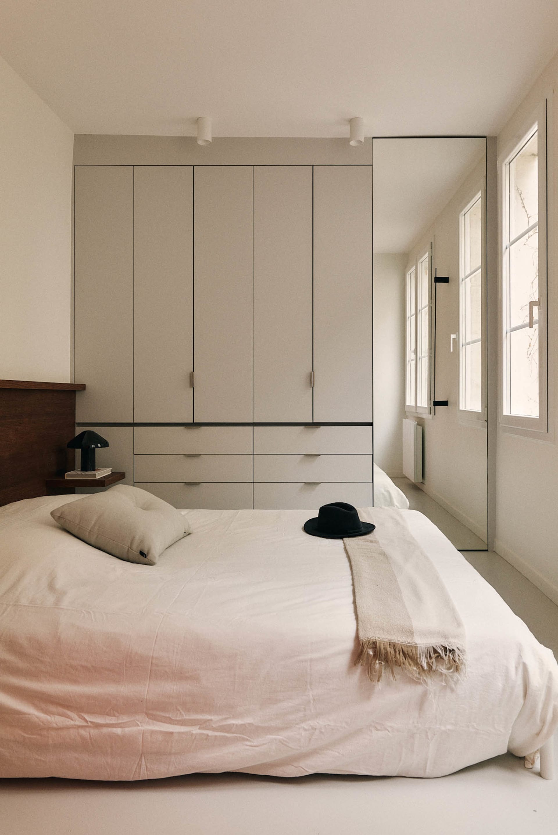 A cozy bedroom with a bed in the center, a hat on the bed, and a window on the right side, providing natural light