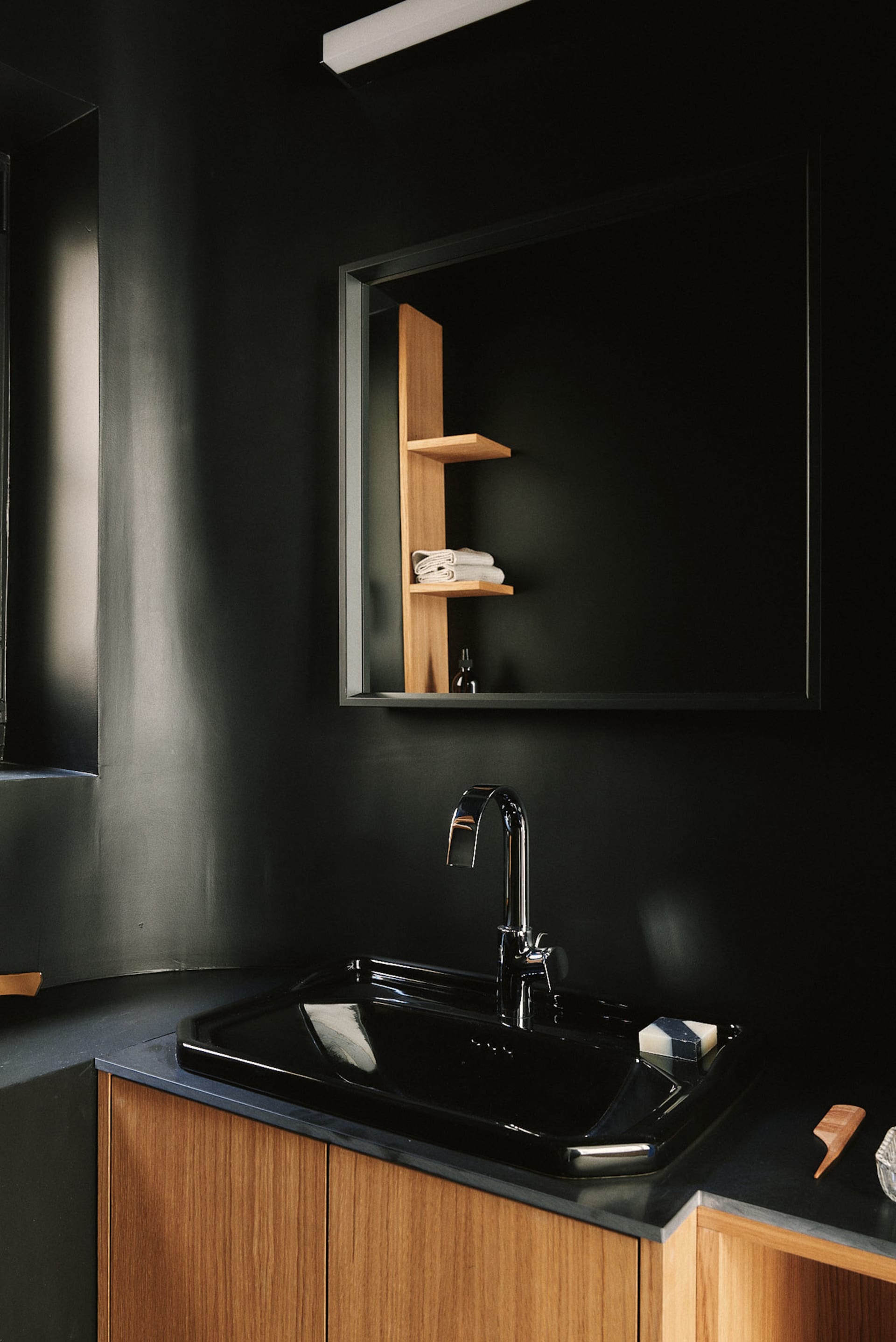 A black sink and mirror are the focus in a dark bathroom setting