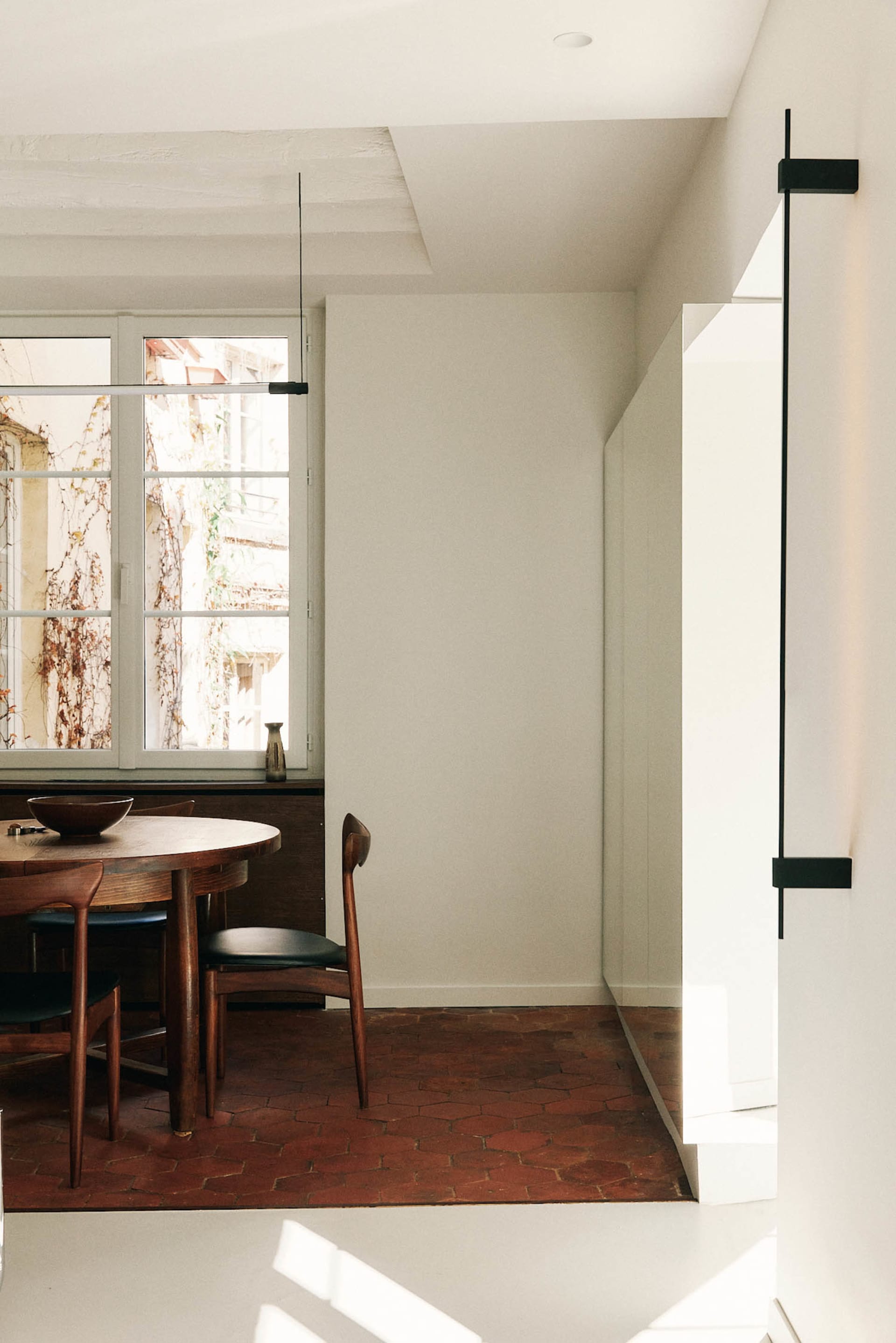 A dining room with a wooden table and chairs, a bowl on the table, and a window, creating a warm and inviting atmosphere