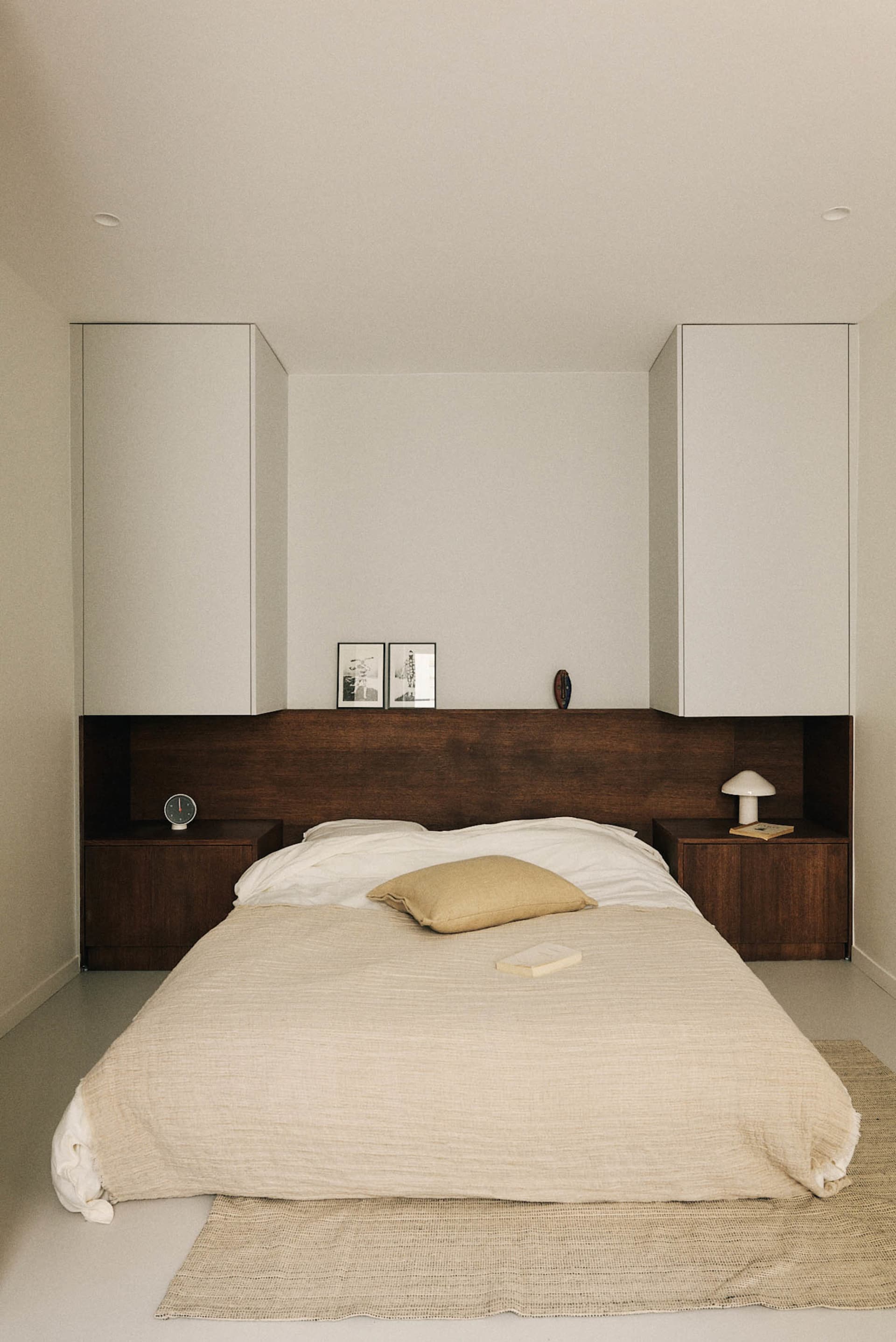 A well-lit bedroom with a bed, nightstand, and dresser, featuring a white comforter, brown pillow, and wooden furniture