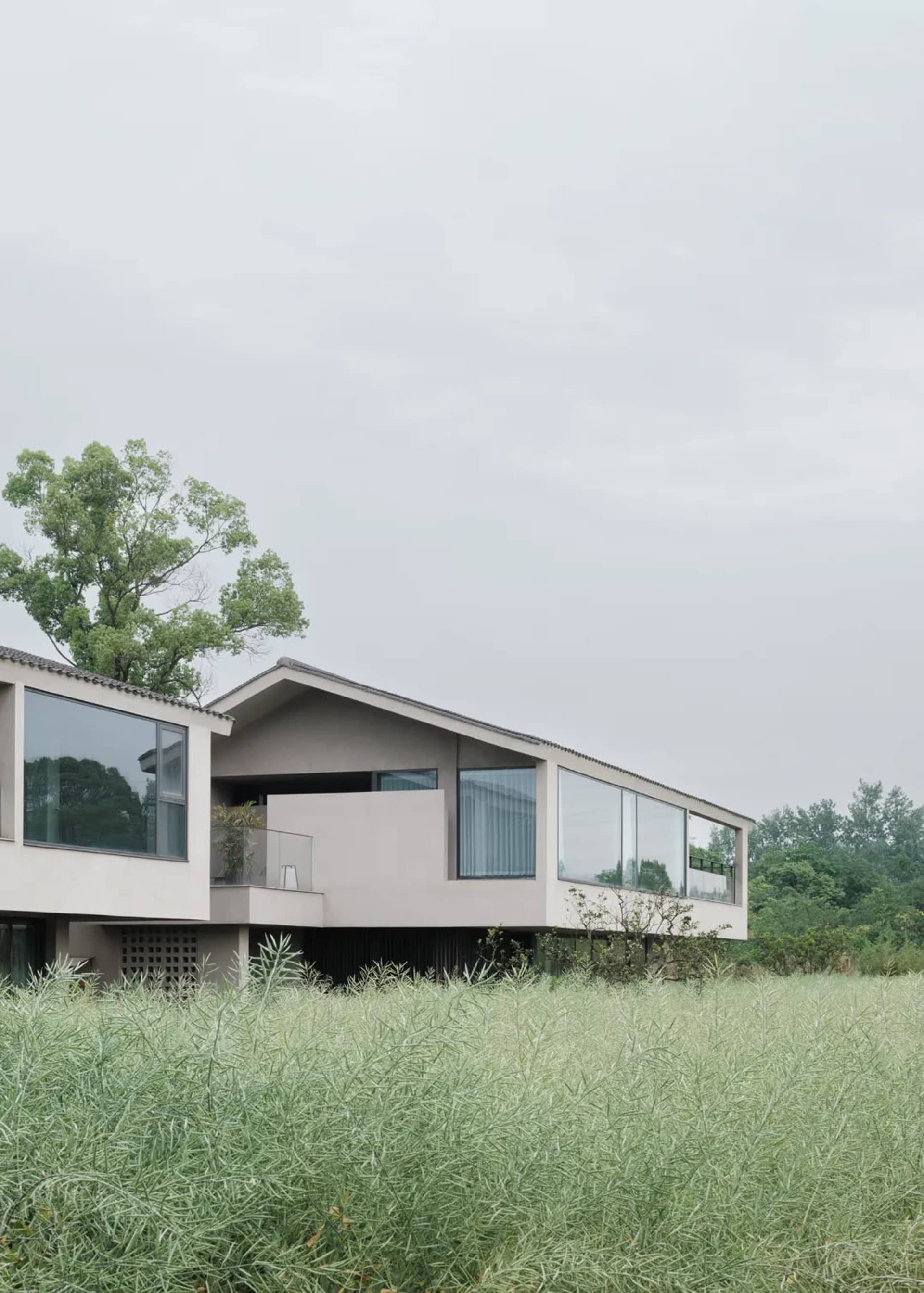 A modern house with a white exterior, sloping roof, and large window, surrounded by a grassy area, with natural light and a serene atmosphere
