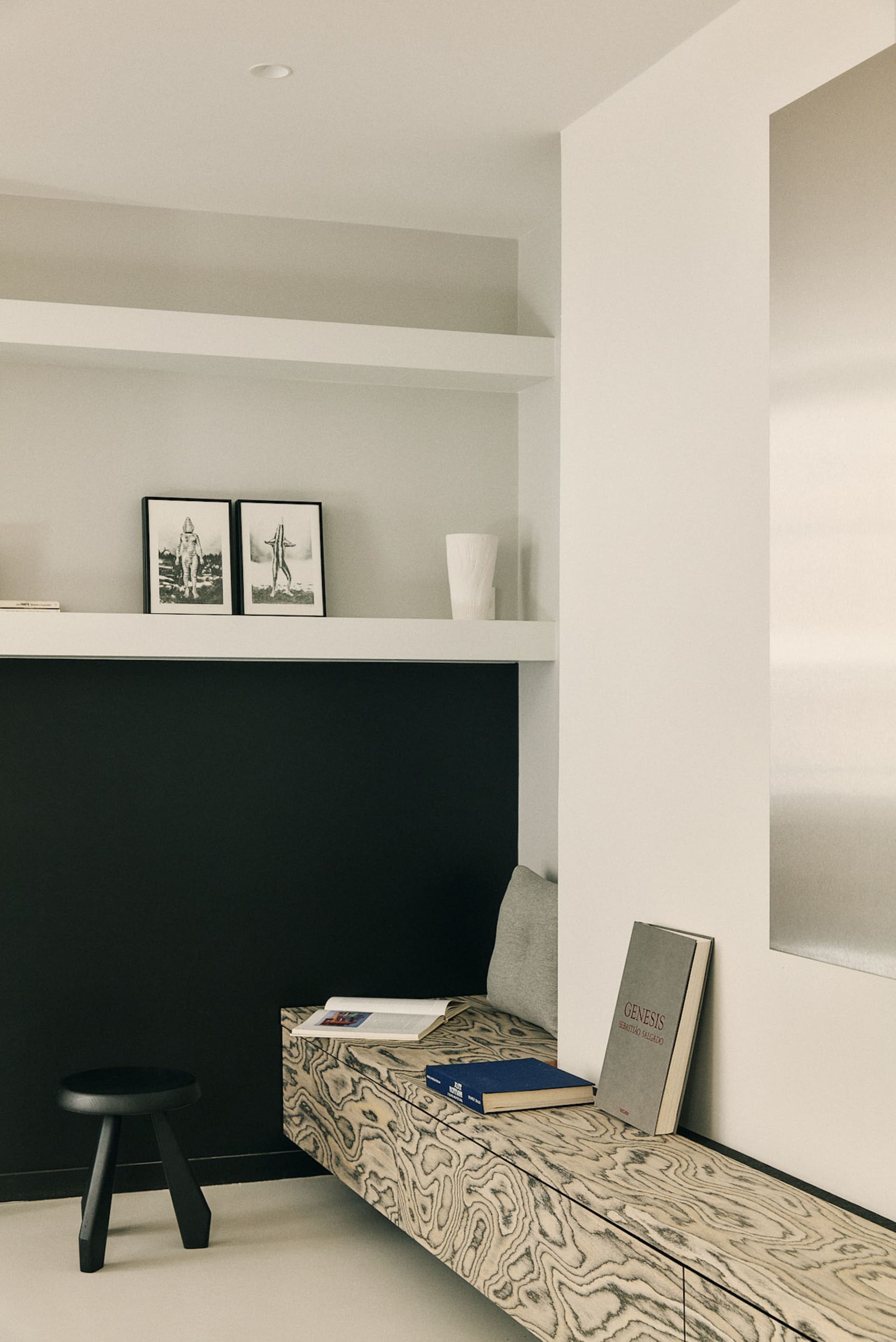 Cozy modern living space with a black wall, white shelf, couch, chair, bookshelf, and vase, lit by dim lighting