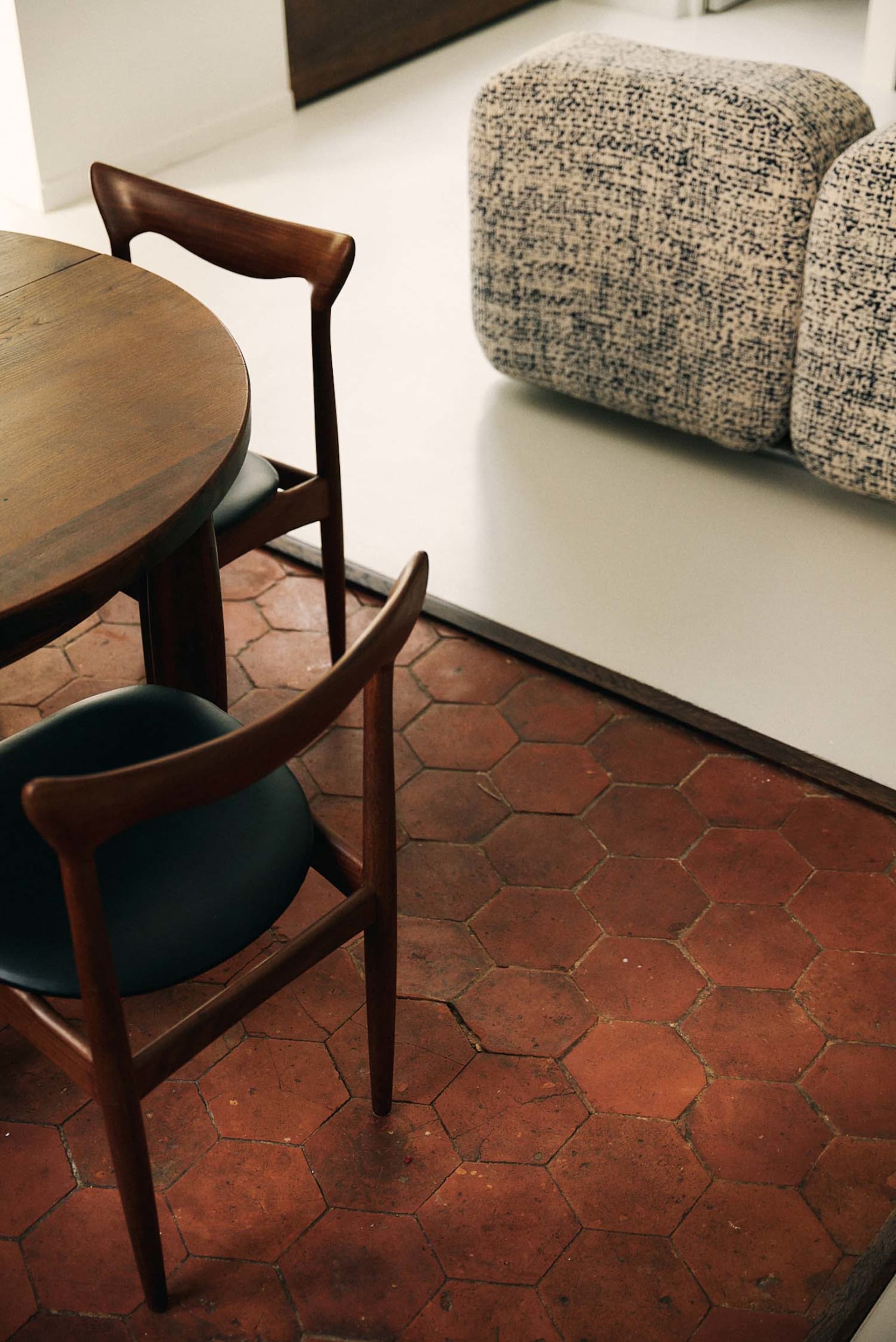 Dimly lit dining room with a wooden table, black chairs, and a tiled floor, featuring a couch, chair, and bench