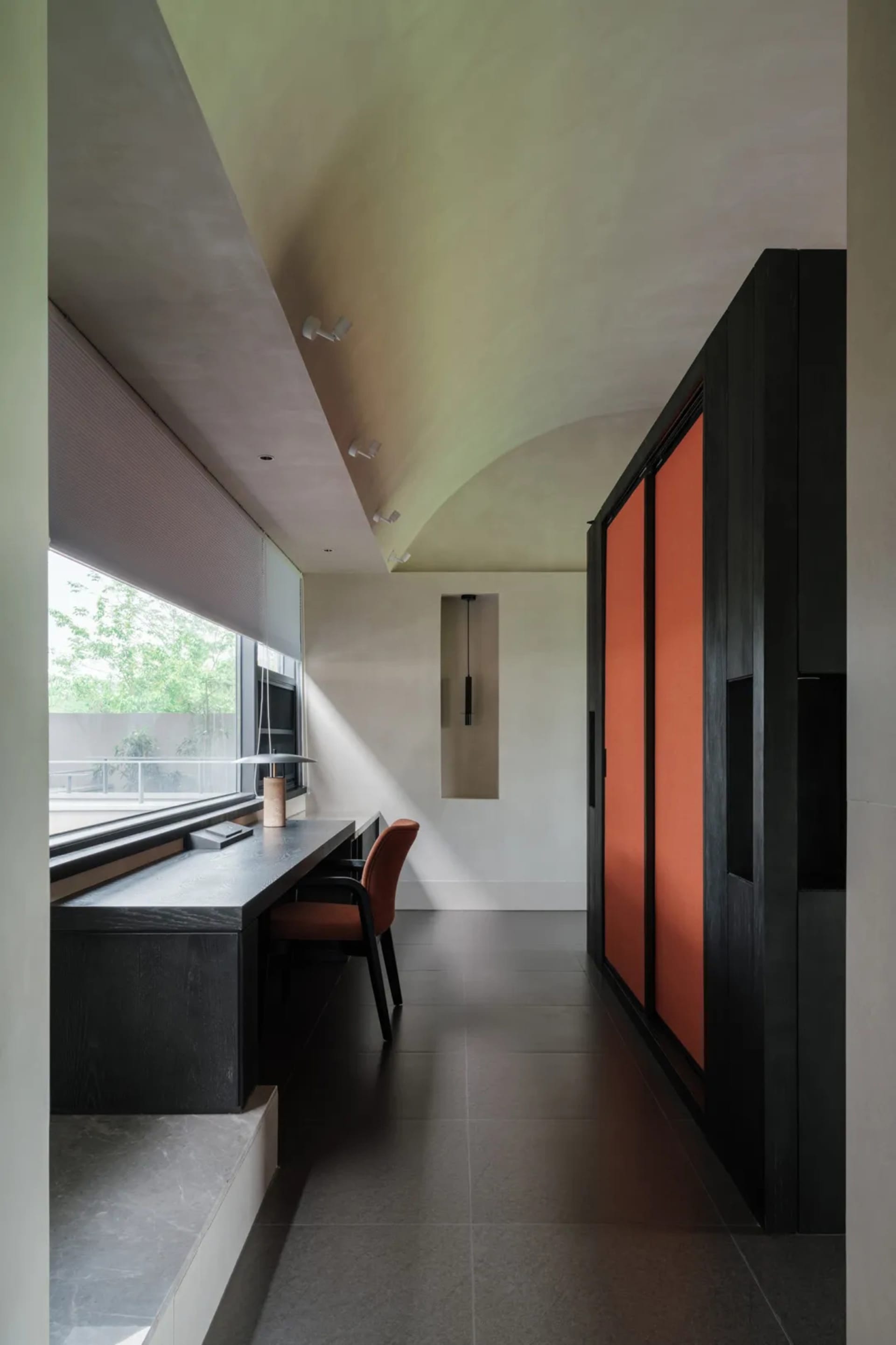 A modern living space with a black and orange color scheme, featuring a desk, chair, closet, and window