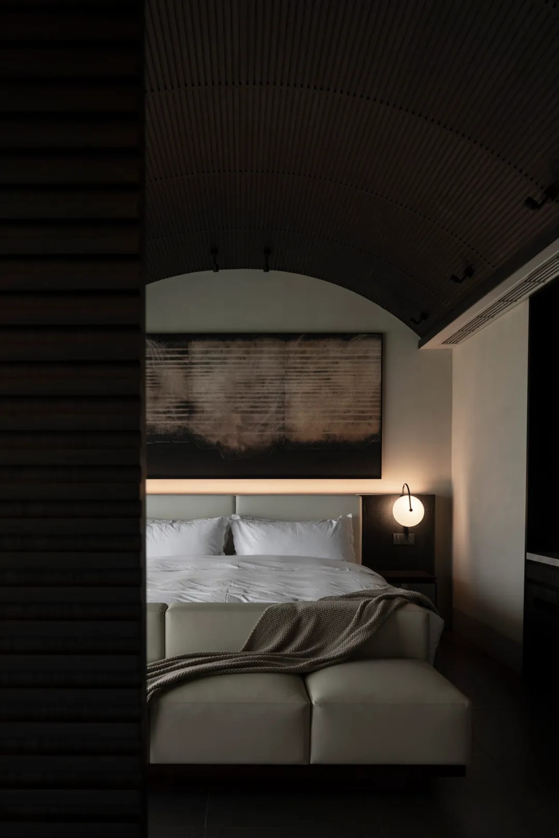 Cozy bedroom with a bed, lamp, and painting, dimly lit with a modern style and minimalist aesthetic
