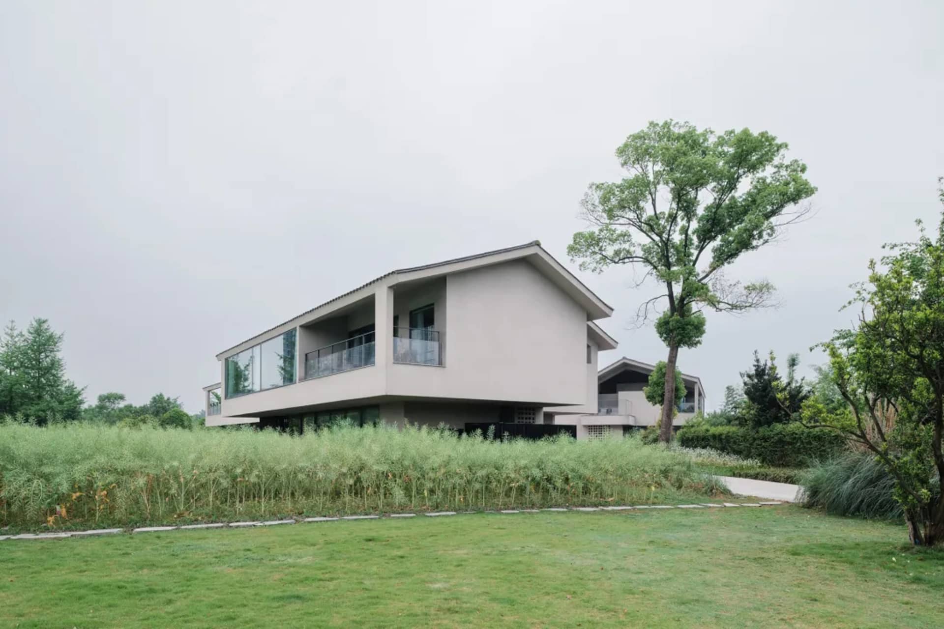 A modern house with a white exterior, surrounded by a lush green field, featuring a large window and several smaller windows, with natural light streaming in