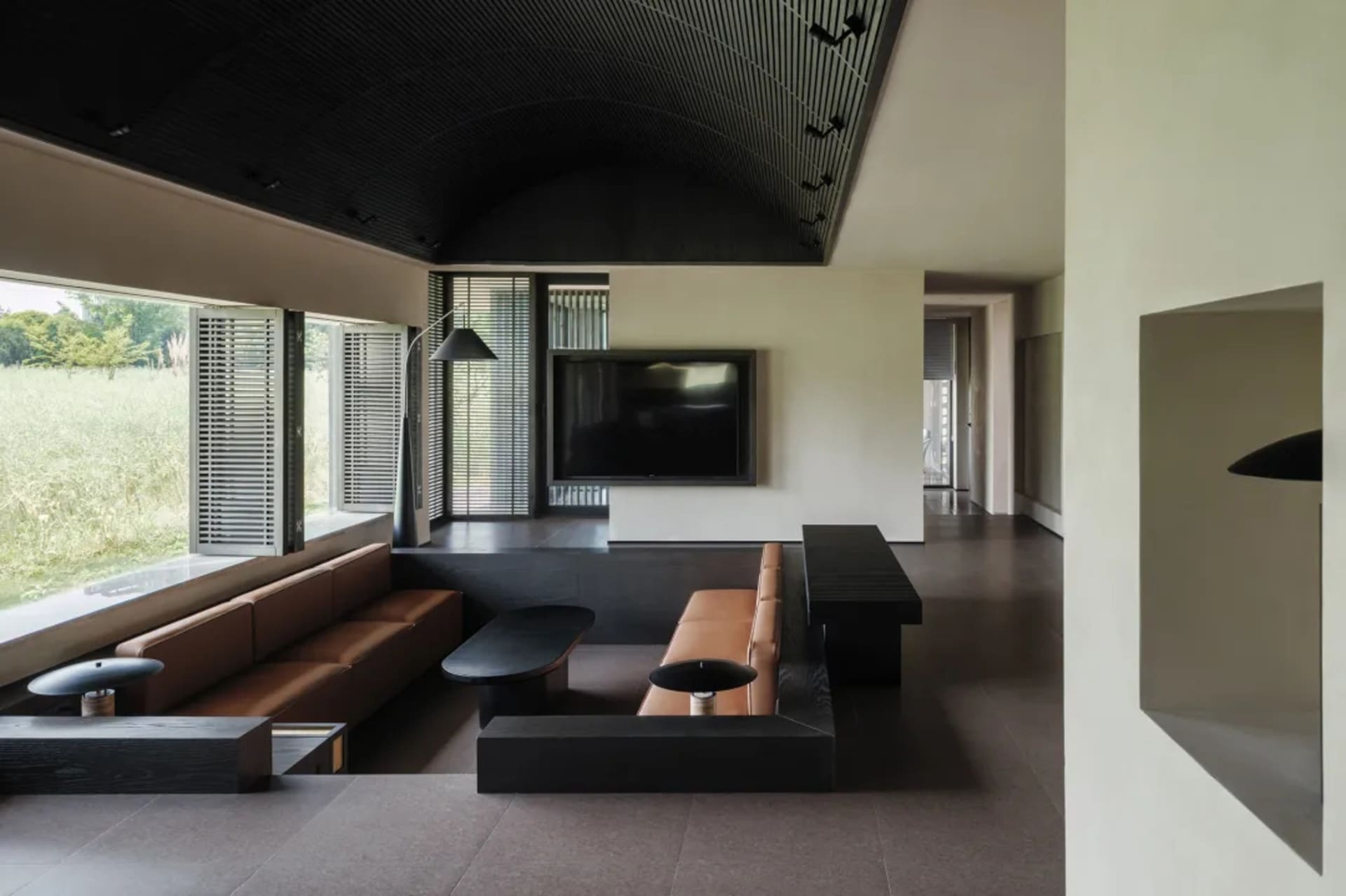 Cozy living room with a black and brown color scheme, a flat screen TV, a couch, and a dining table, featuring wood and leather materials and natural light from the windows