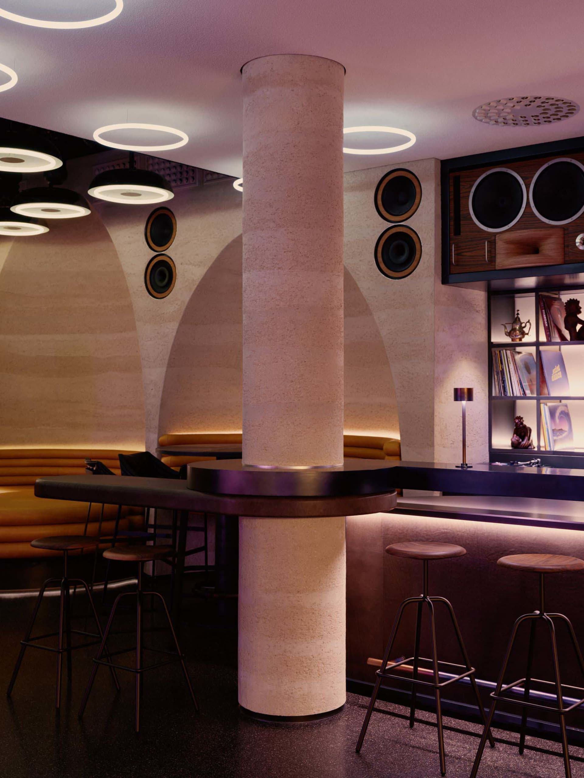 A modern bar with a mix of wood and metal materials, featuring a counter, pillar, and comfortable seating for guests