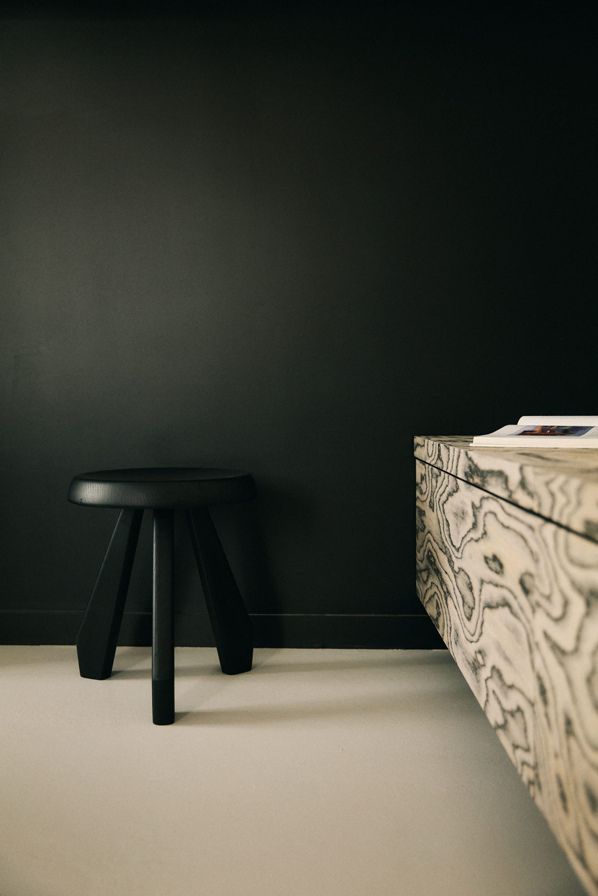 A minimalist bedroom with a black chair and table, a bed in the background, and dim lighting creating a cozy atmosphere