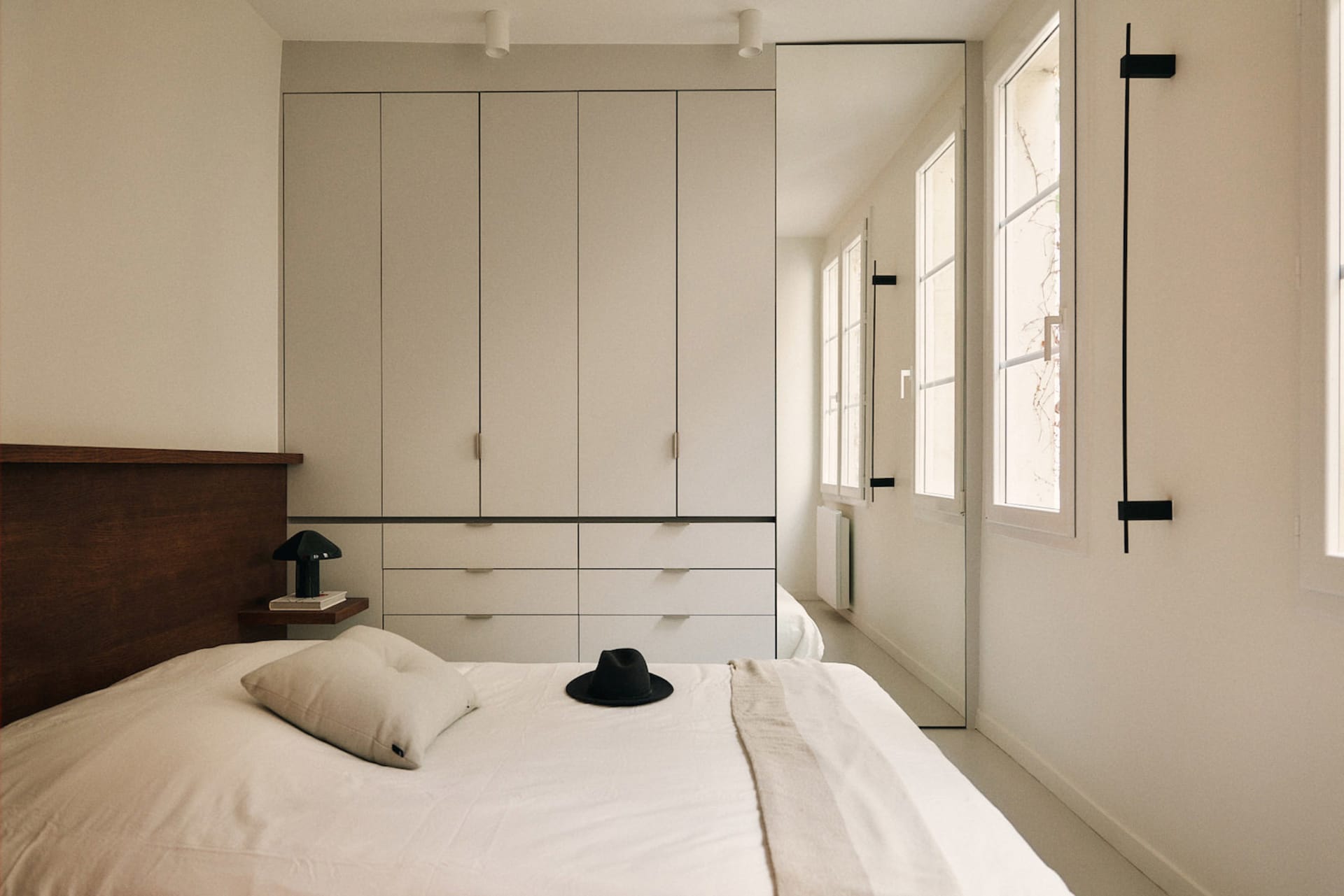 A minimalist bedroom with a white bed, dresser, and natural light from an open window