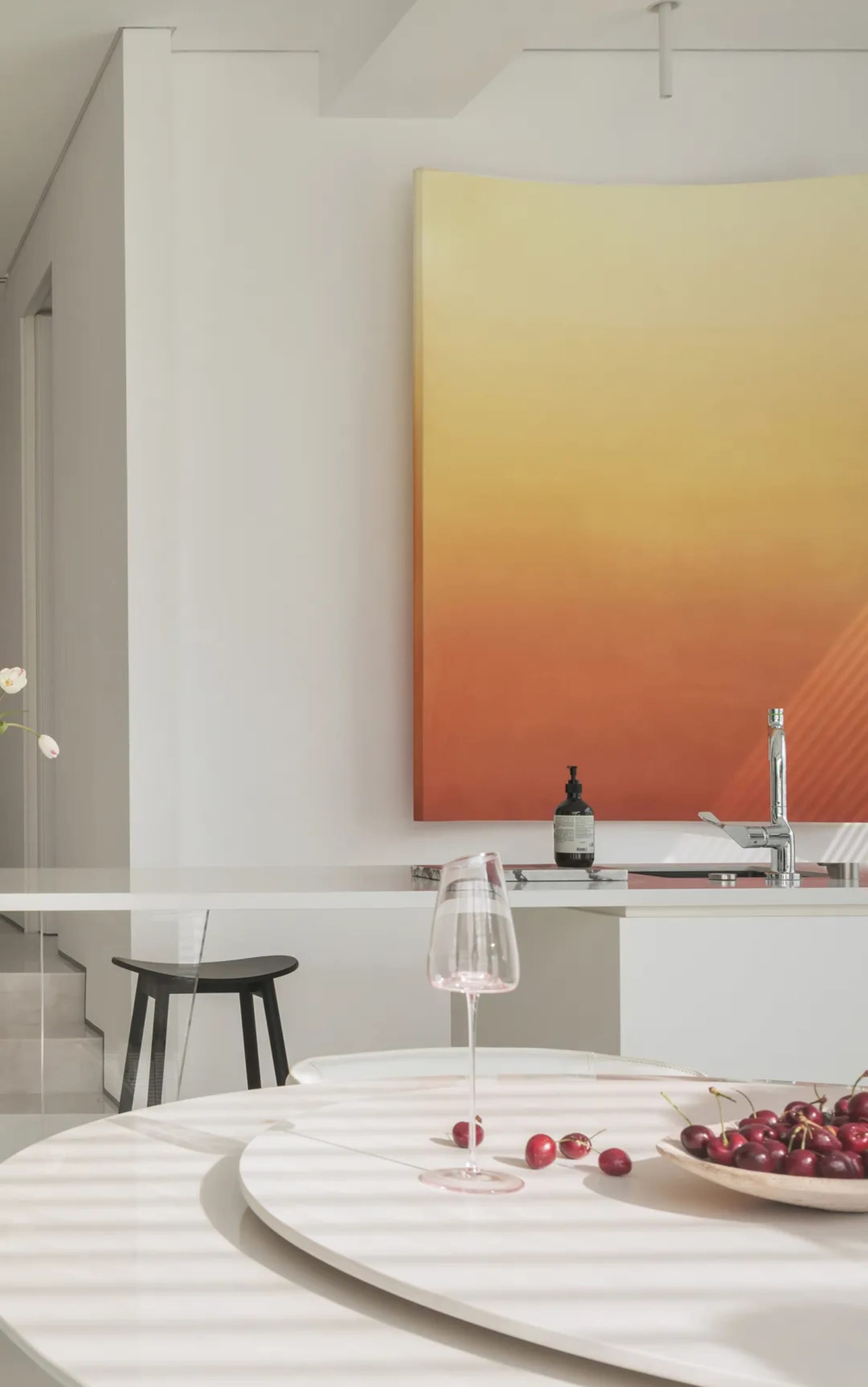 Cozy modern living space with a dining table, a couch, a chair, and a potted plant, featuring a large painting on the wall and a vase with flowers, set with a wine glass and a bottle of wine