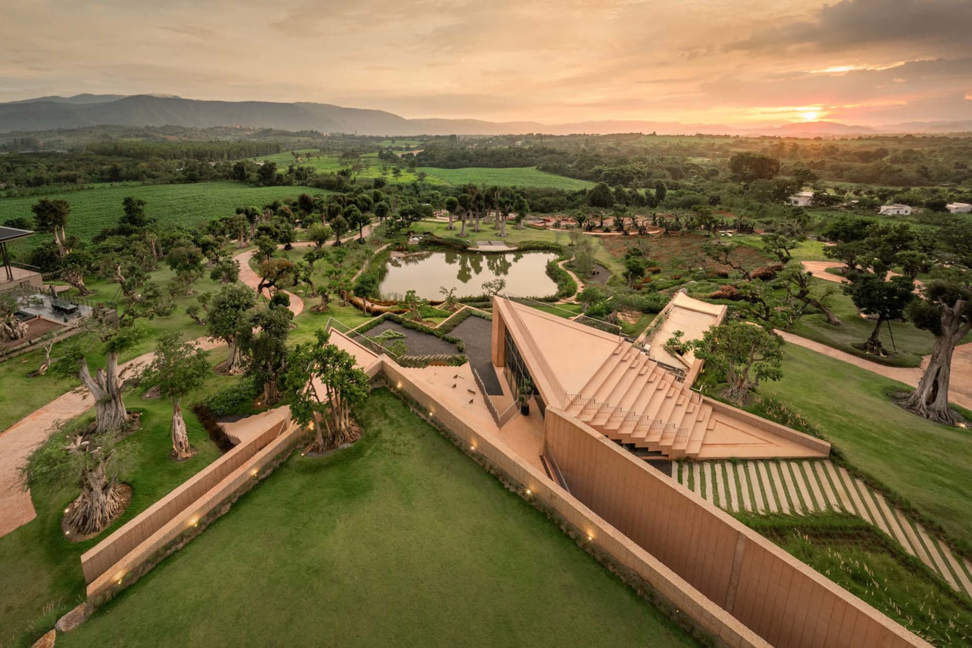 A modern building with a large open courtyard featuring a pond, surrounded by the building with a mix of concrete and wood architecture, taken during sunset