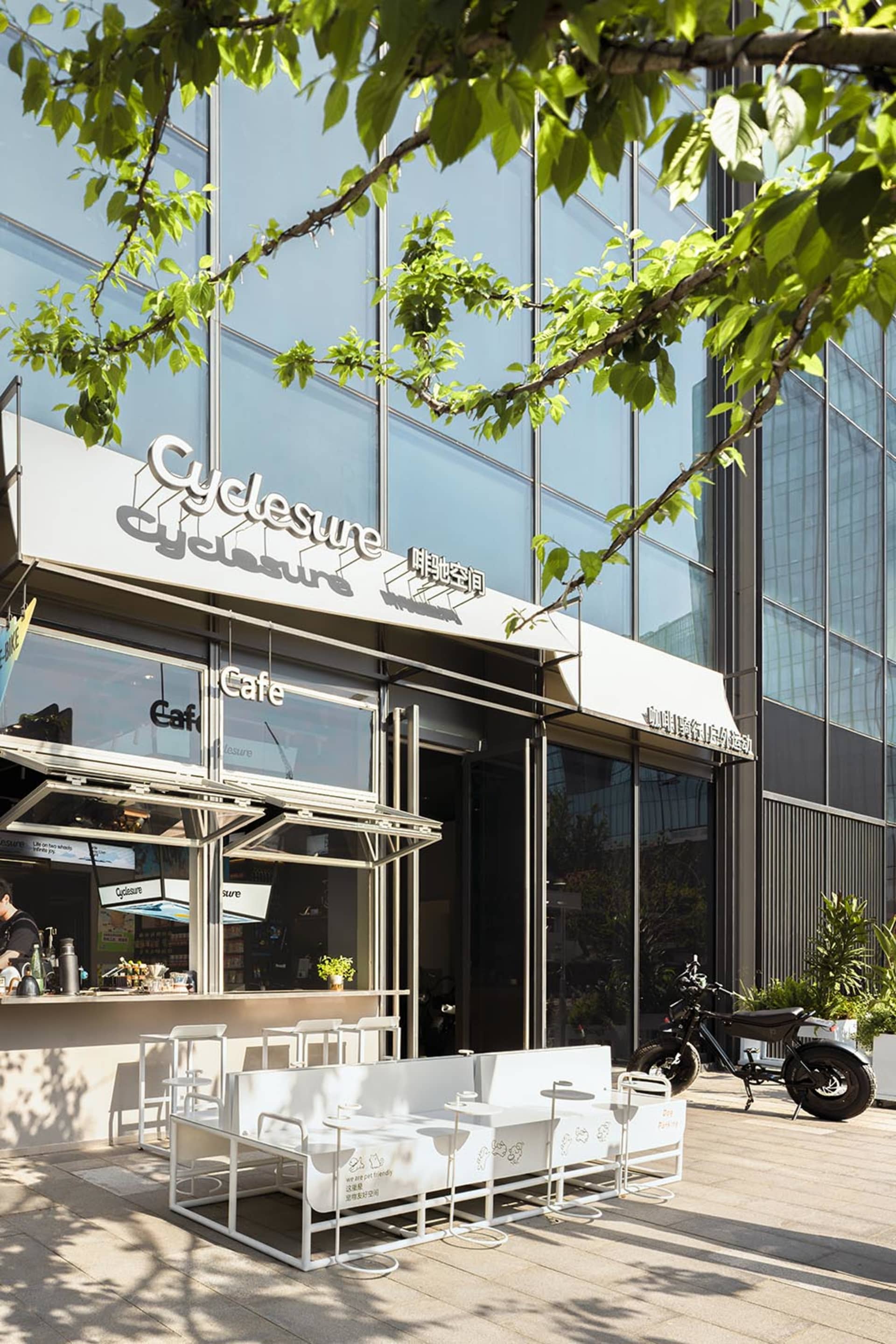 A modern cafe with a white facade, a motorcycle parked outside, and natural light pouring in through the windows