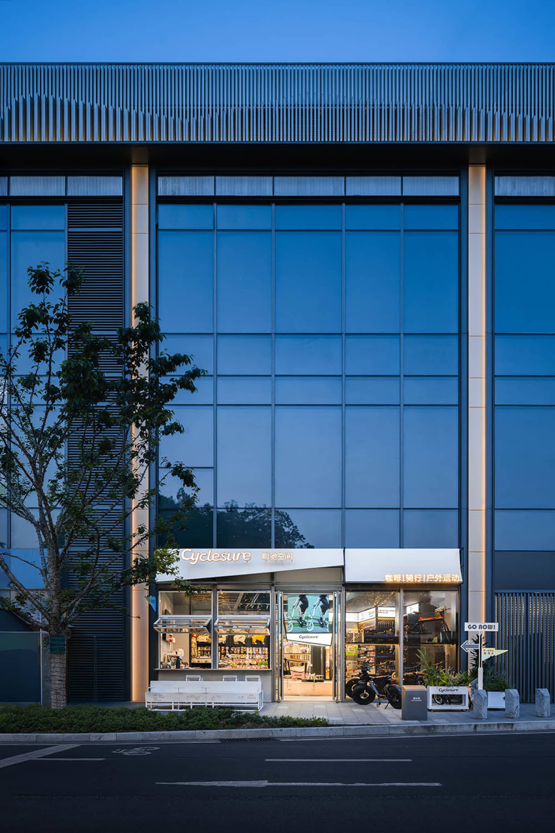 A modern storefront with a large window and door, featuring a motorcycle parked outside, set against a predominantly blue background with natural light creating a bright and inviting atmosphere